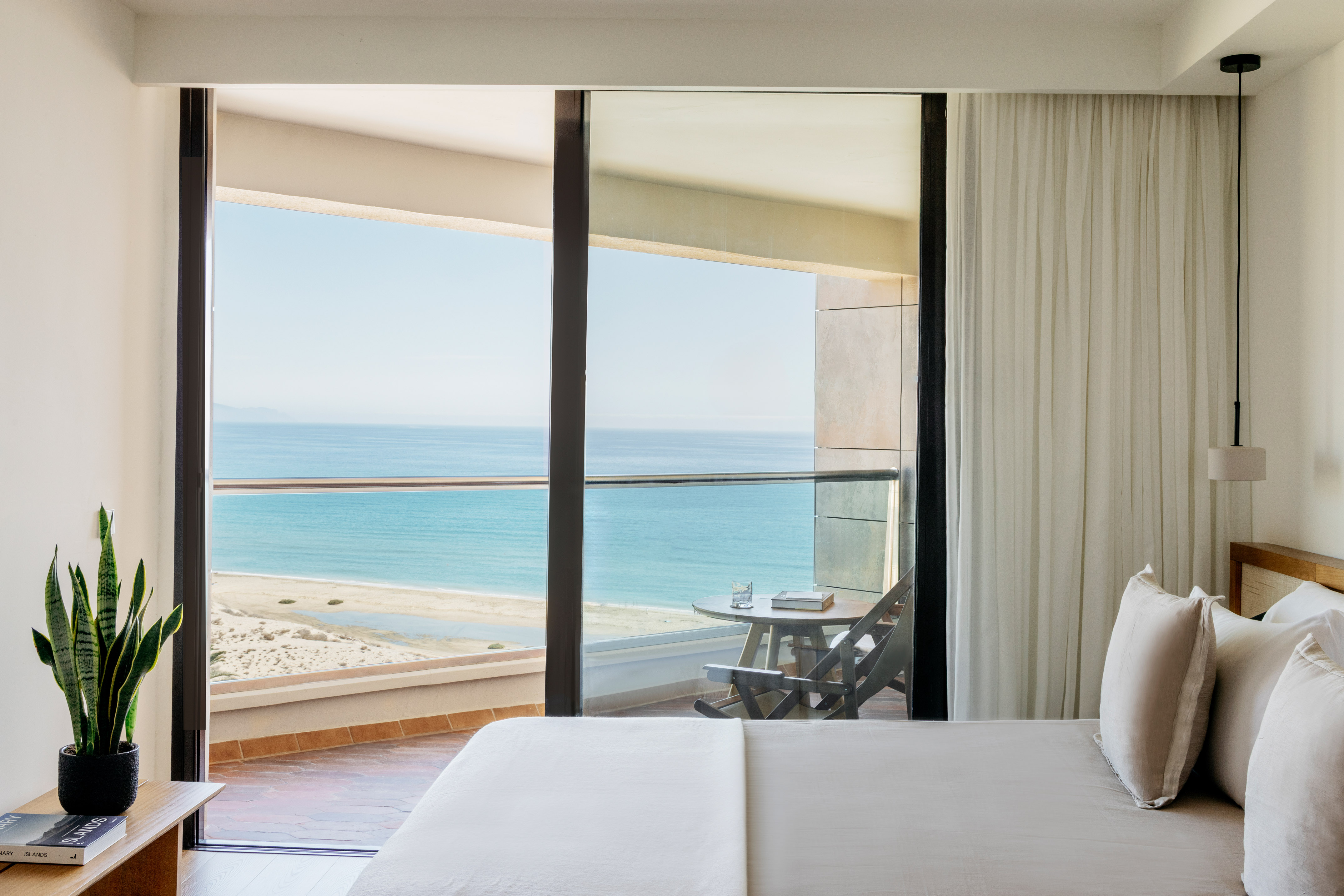 Modern bedroom with ocean view balcony and sandy beach.