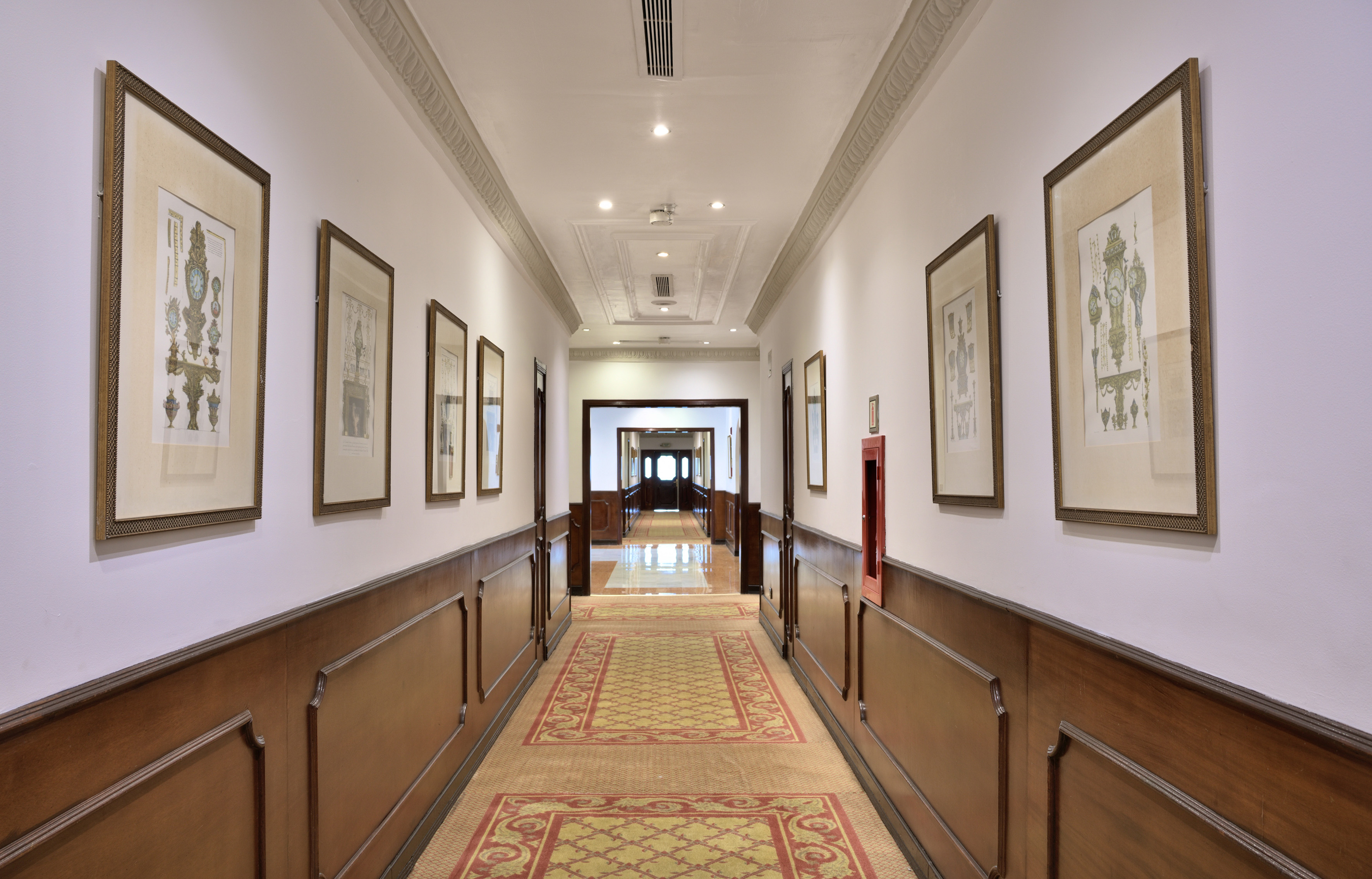 Elegant hotel hallway with framed art, wood wainscoting, and patterned carpet.