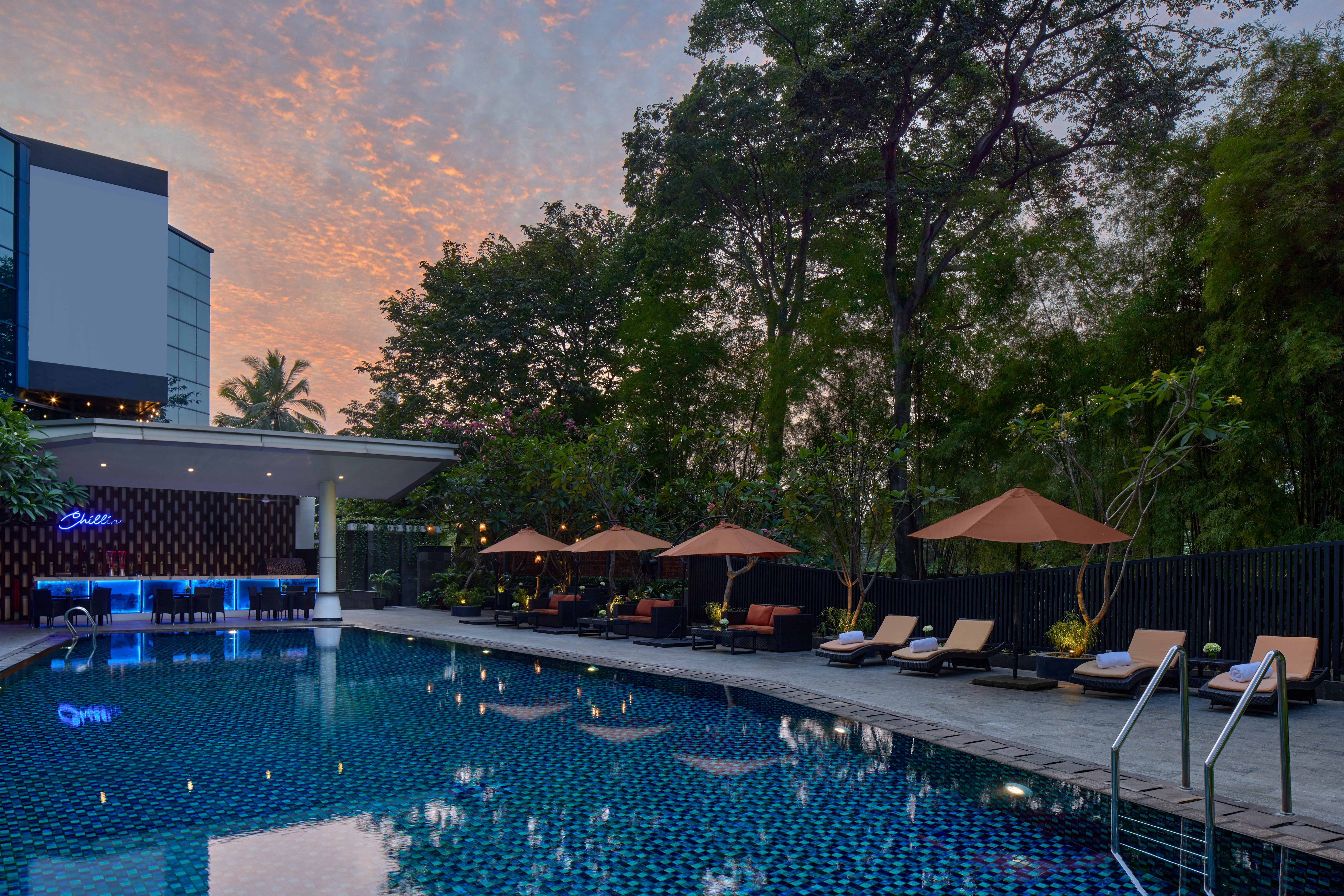 Resort swimming pool with glowing bar, lounge chairs, and sunset sky.