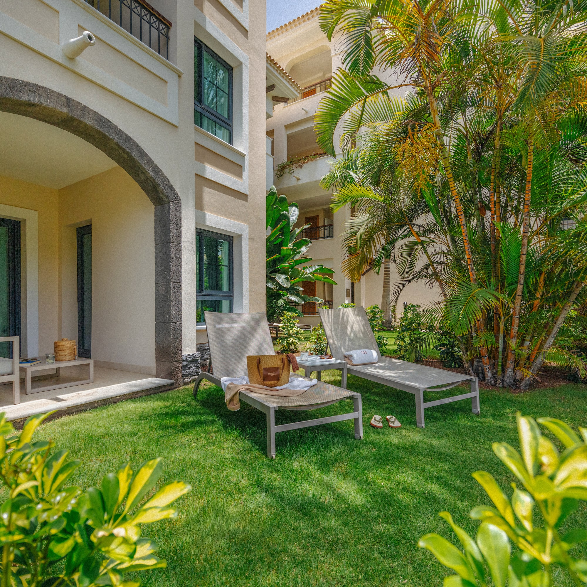 Ground-floor resort patio with lounge chairs on lawn, tropical palm trees.