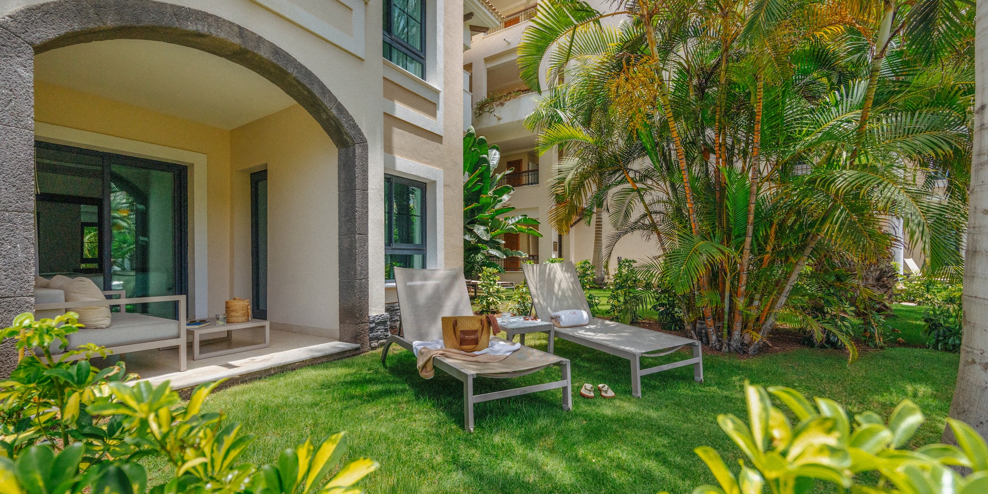Ground-floor resort patio with lounge chairs on lawn, tropical palm trees.