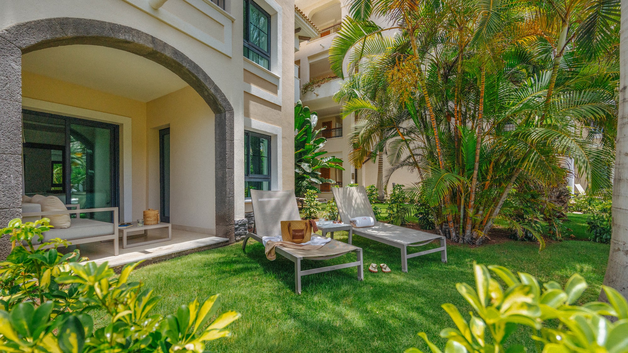 Ground-floor resort patio with lounge chairs on lawn, tropical palm trees.