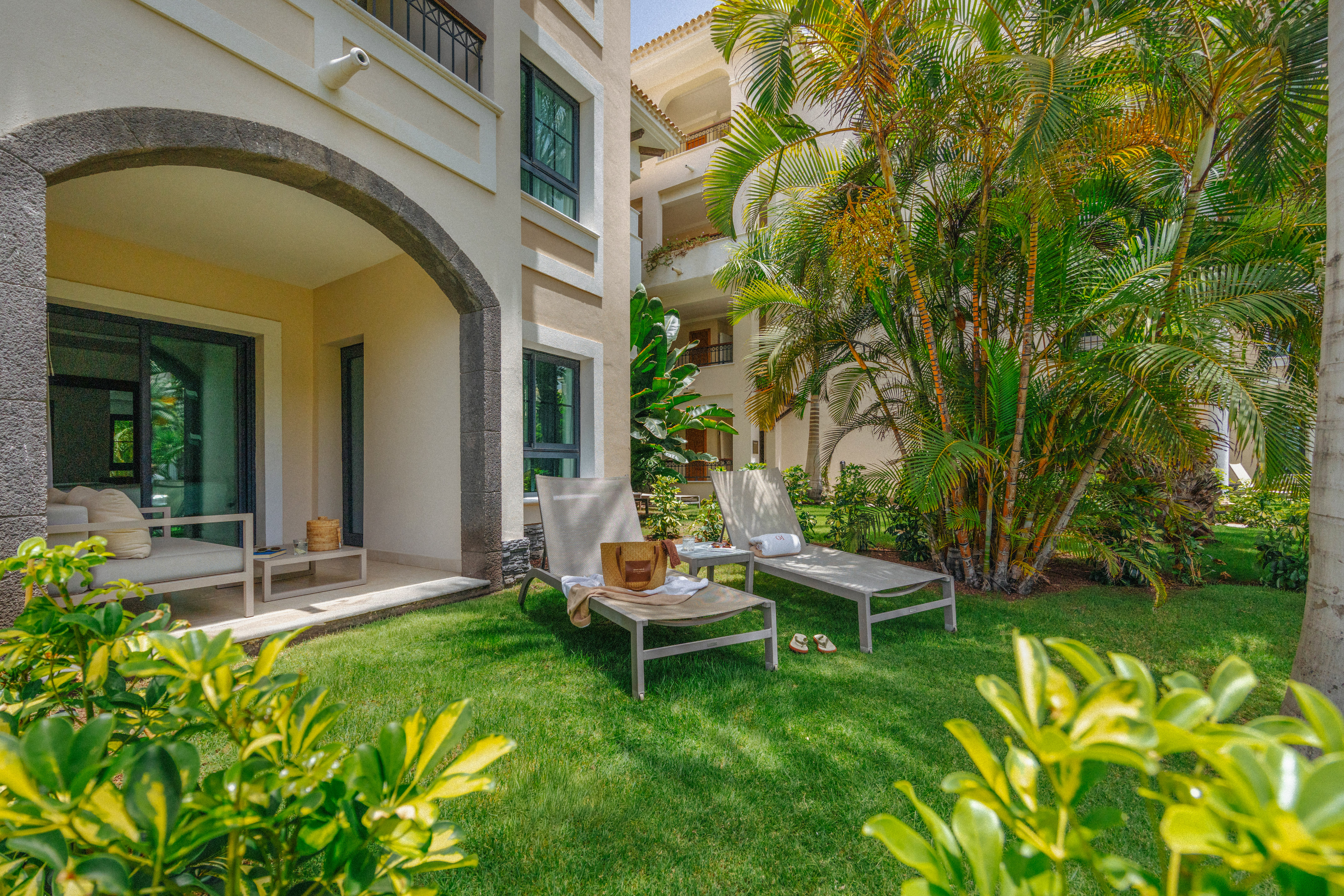 Ground-floor resort patio with lounge chairs on lawn, tropical palm trees.