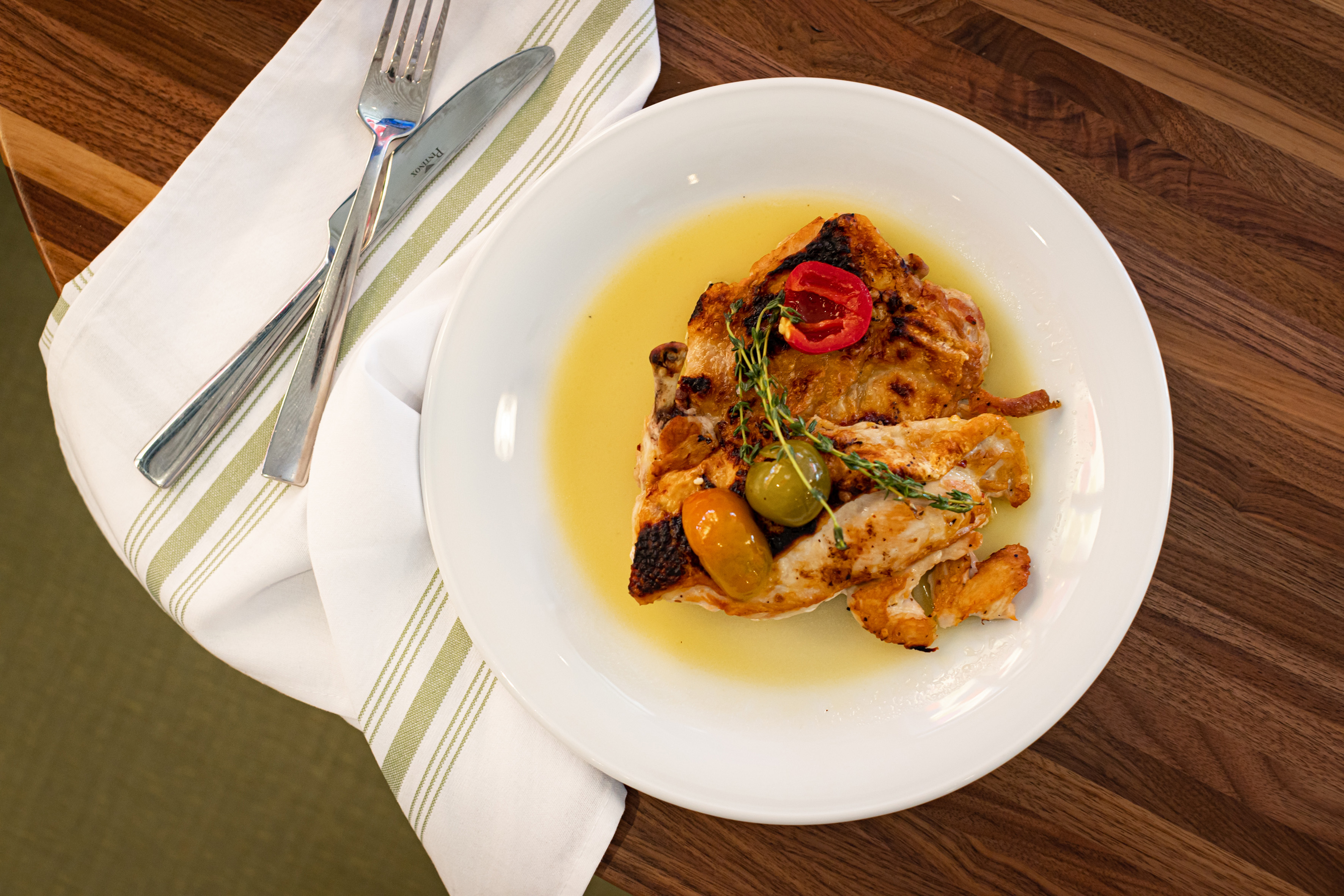 Grilled chicken, cherry tomatoes, fresh thyme, and sauce on a white plate.
