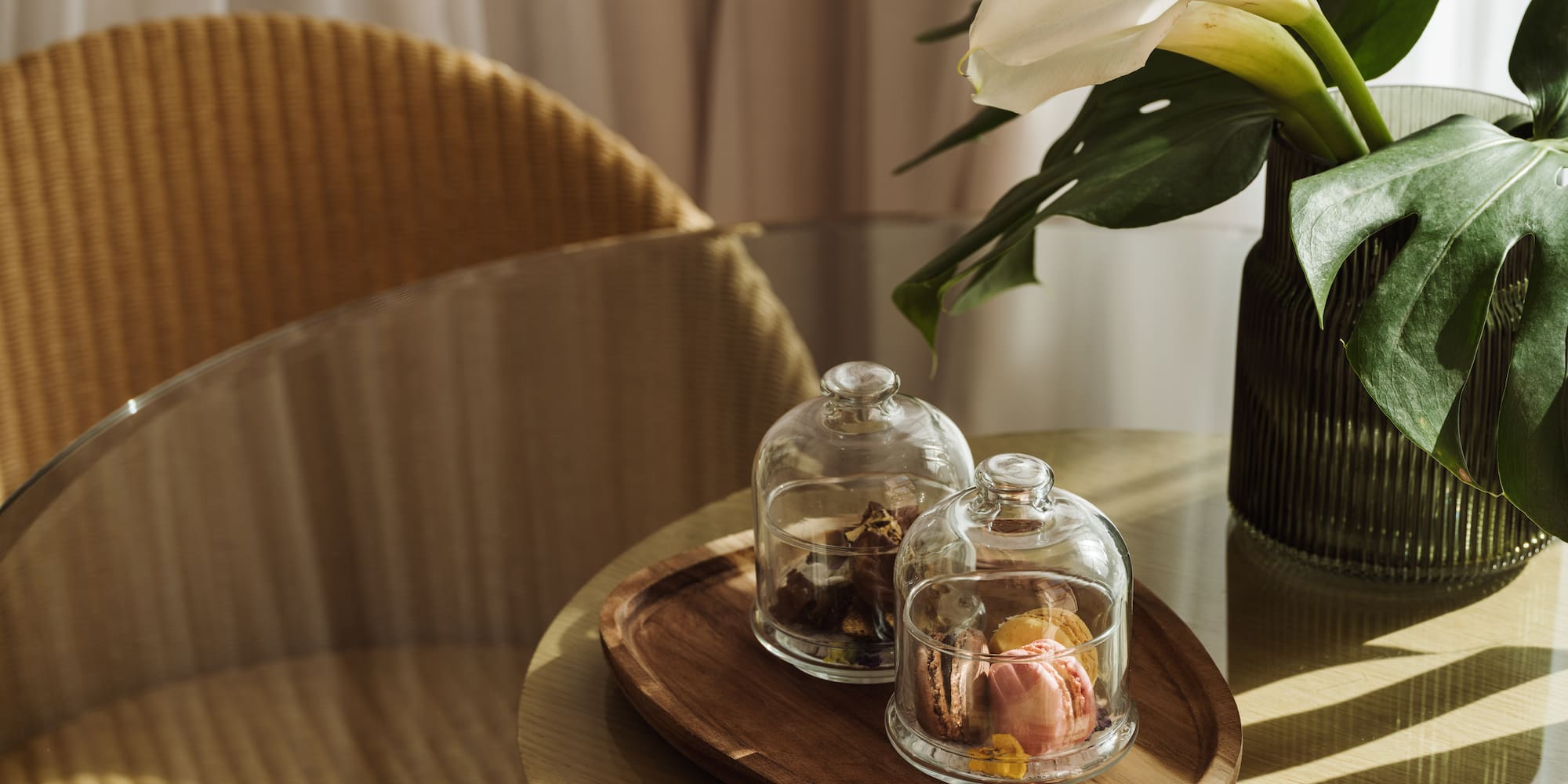 Macarons in cloches, white calla lilies, monstera on a glass side table.