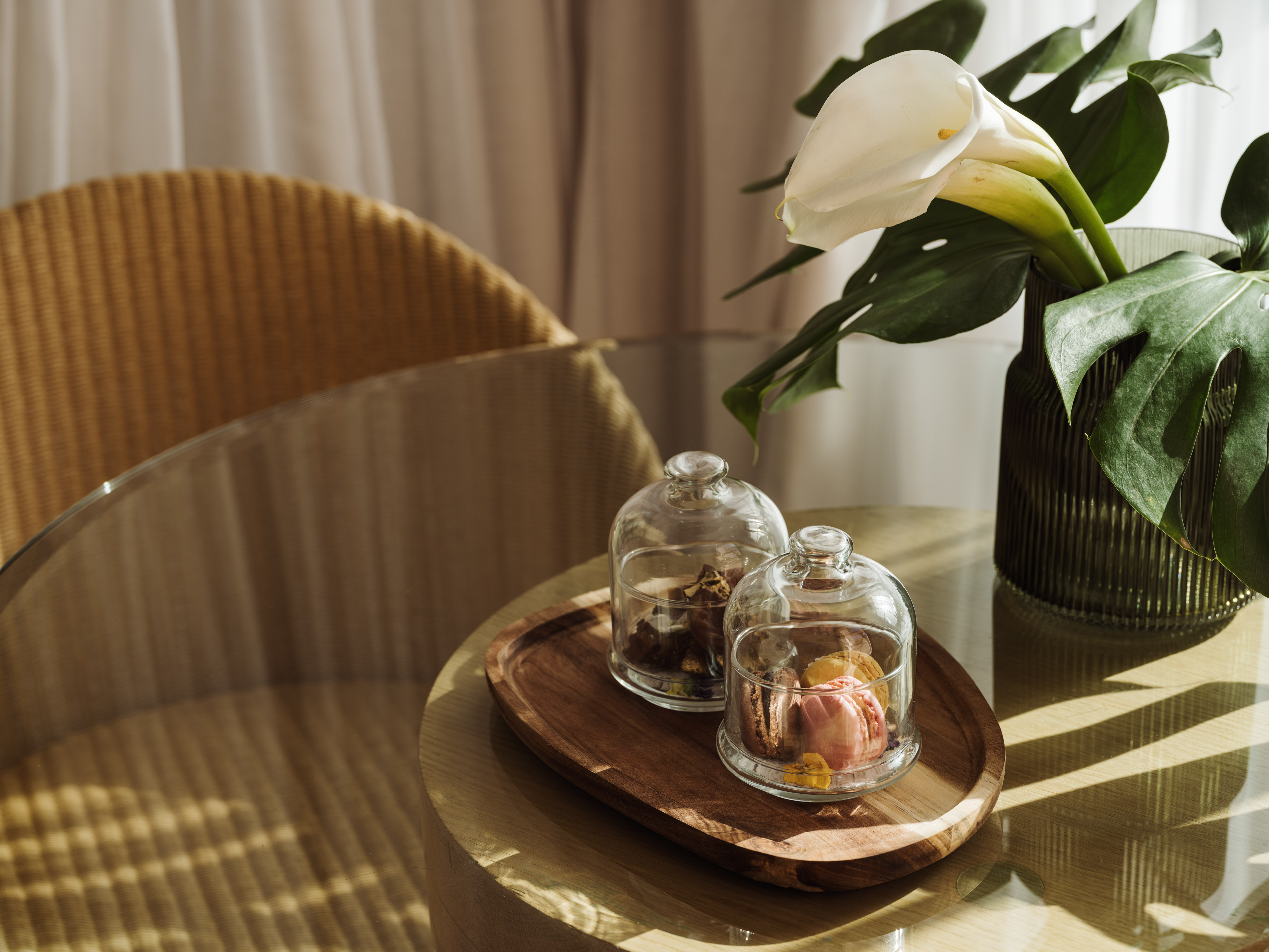 Macarons in cloches, white calla lilies, monstera on a glass side table.