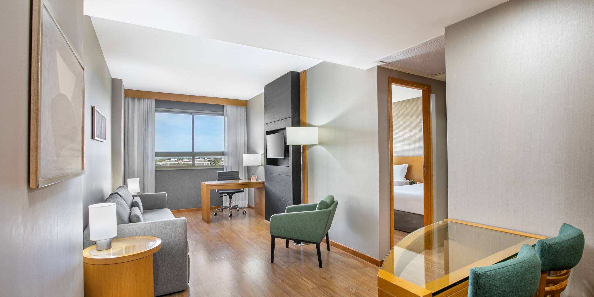 Hotel suite living area with work desk, sofa, and partial view of bedroom.