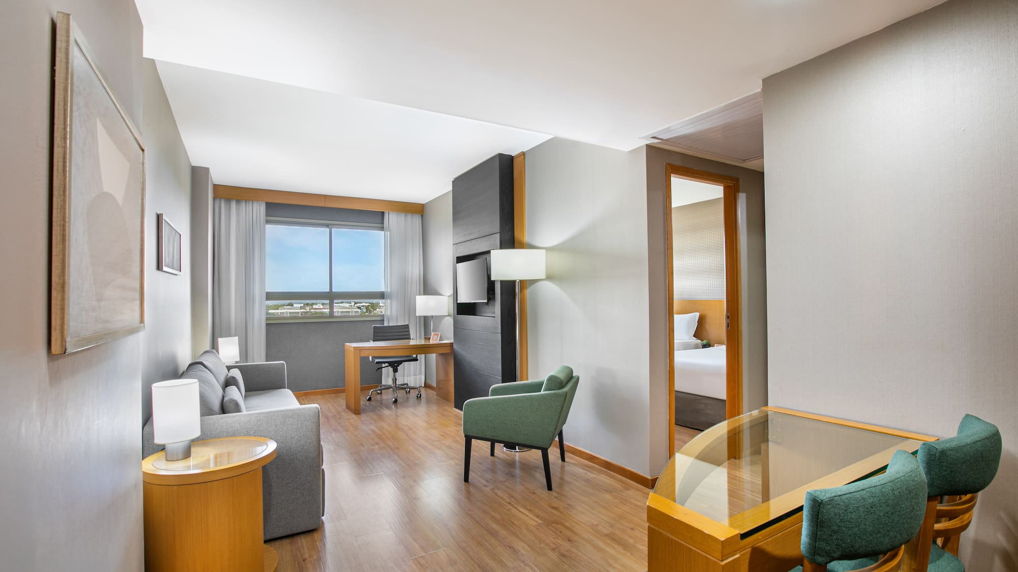 Hotel suite living area with work desk, sofa, and partial view of bedroom.