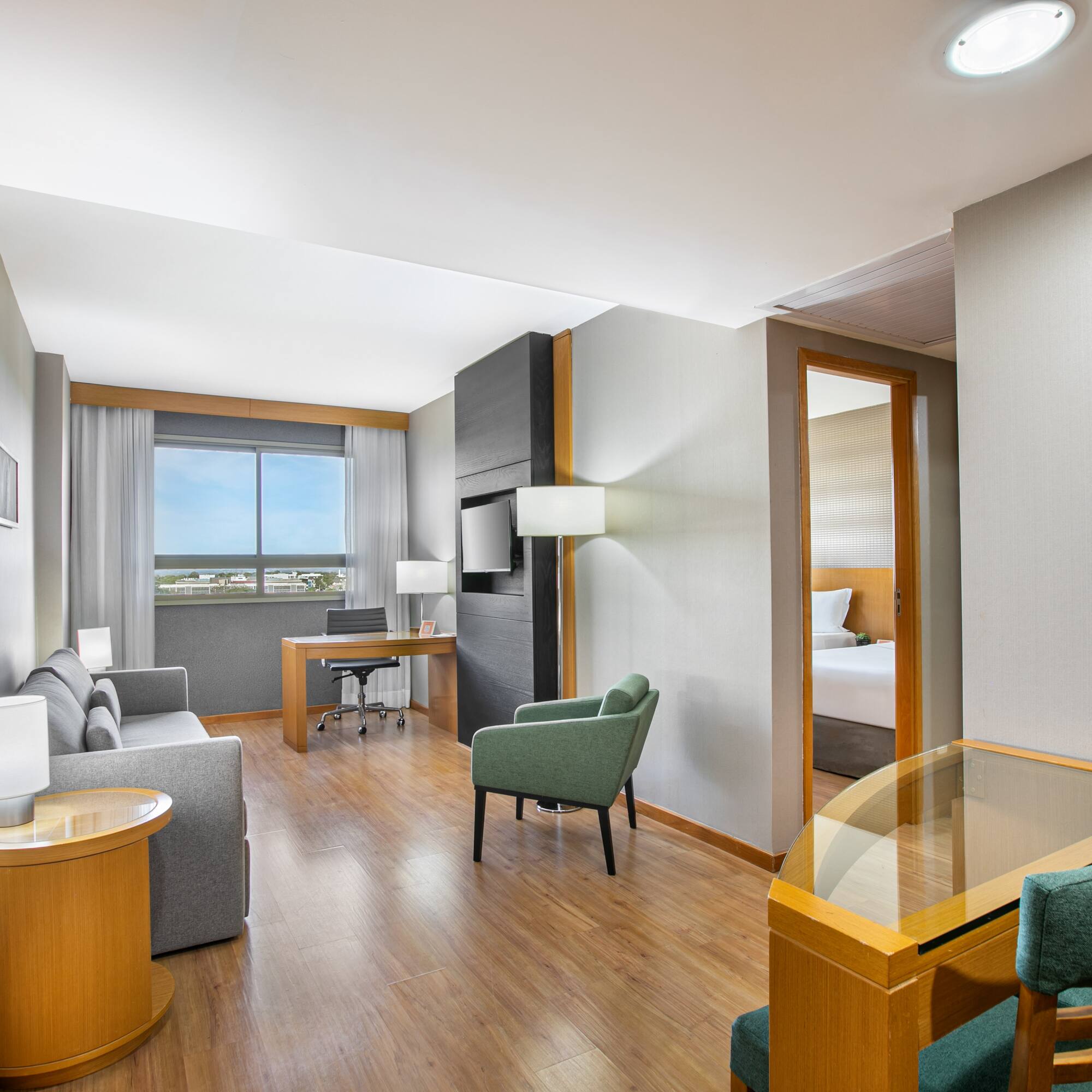 Hotel suite living area with work desk, sofa, and partial view of bedroom.