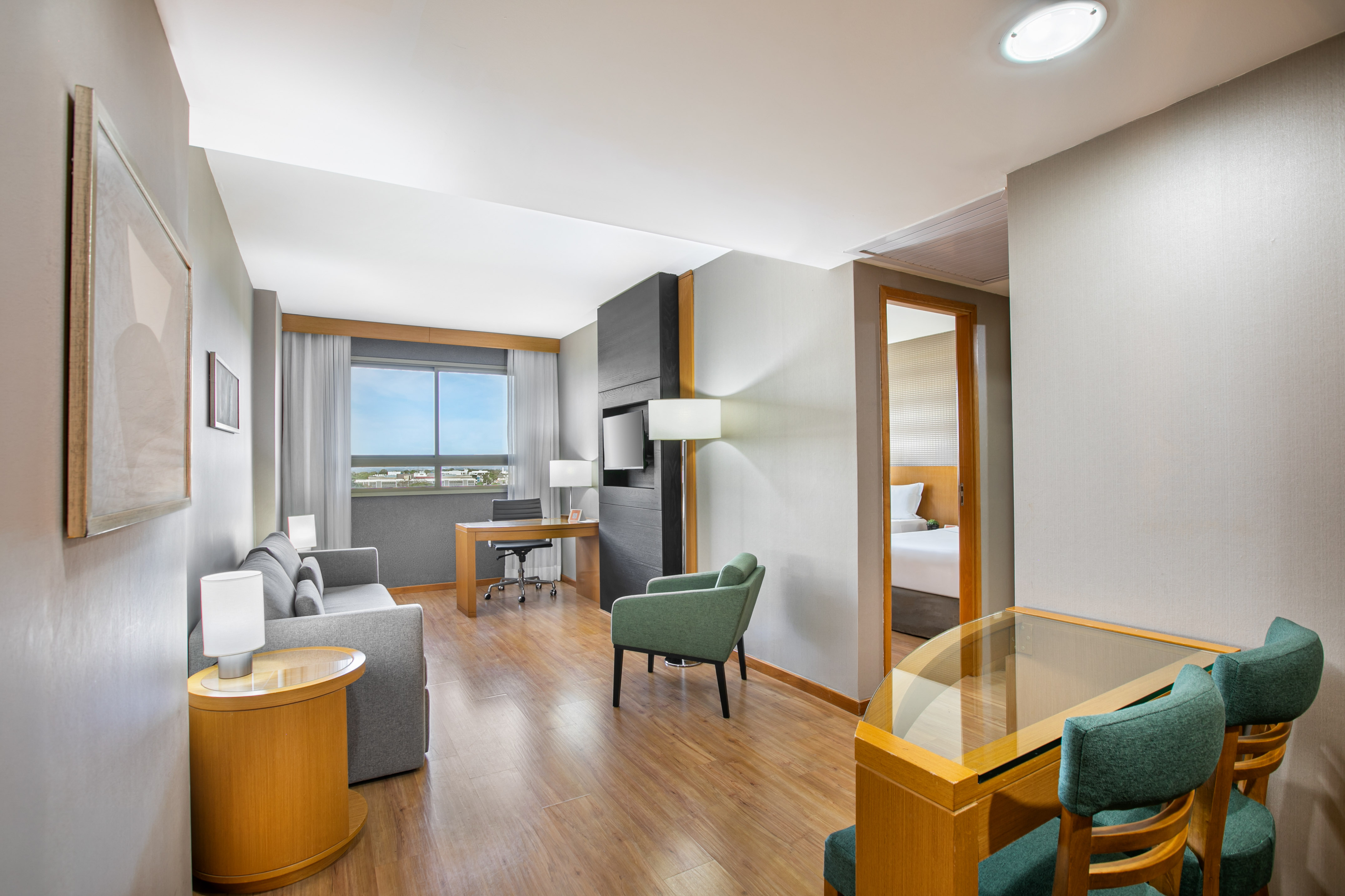 Hotel suite living area with work desk, sofa, and partial view of bedroom.