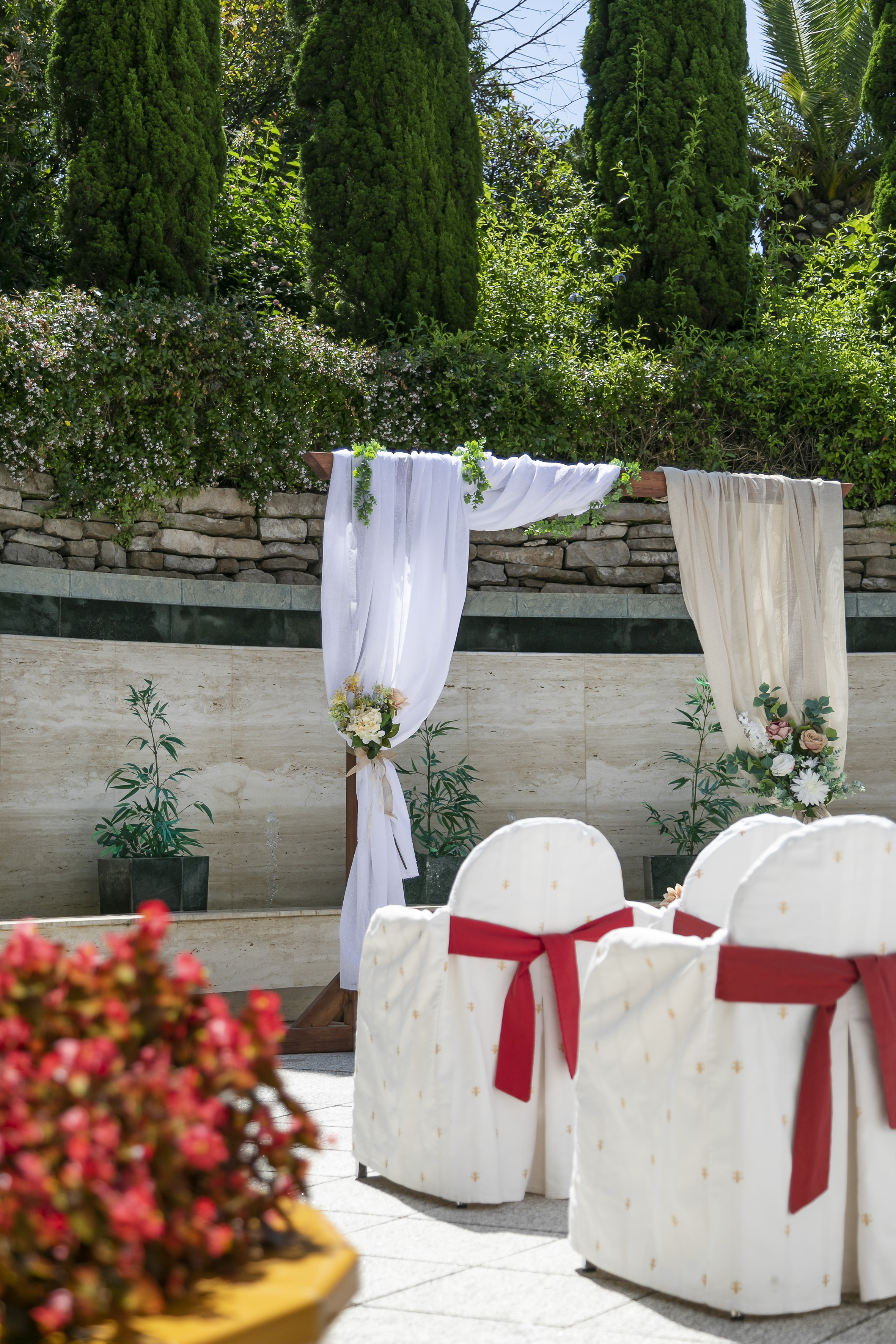 Garden wedding arch with white drapes, floral bouquets, and white chairs.