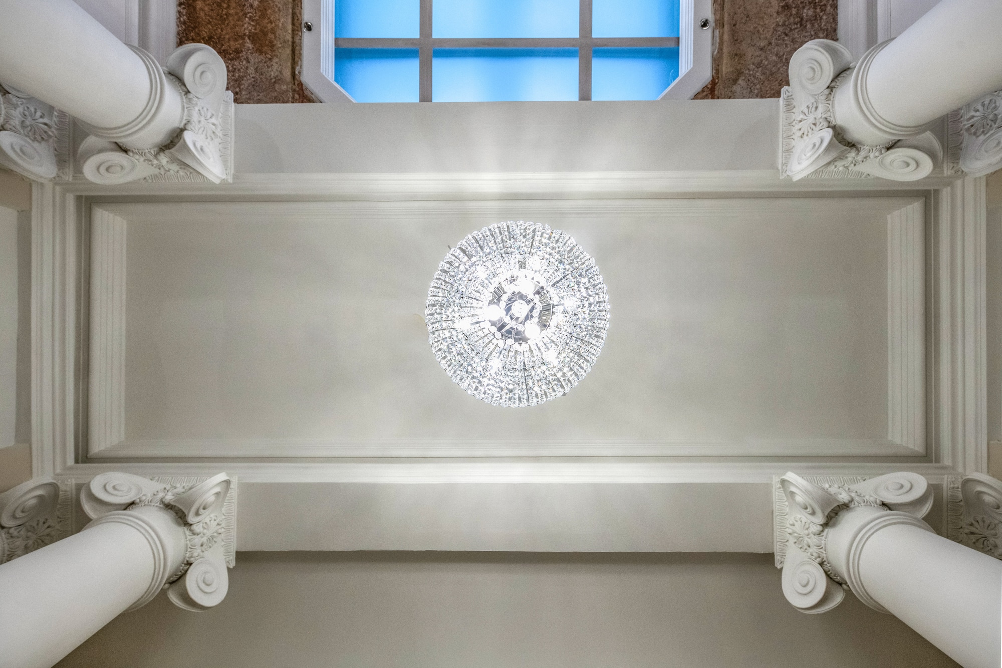Crystal chandelier, ornate ceiling, architectural columns, and skylight.