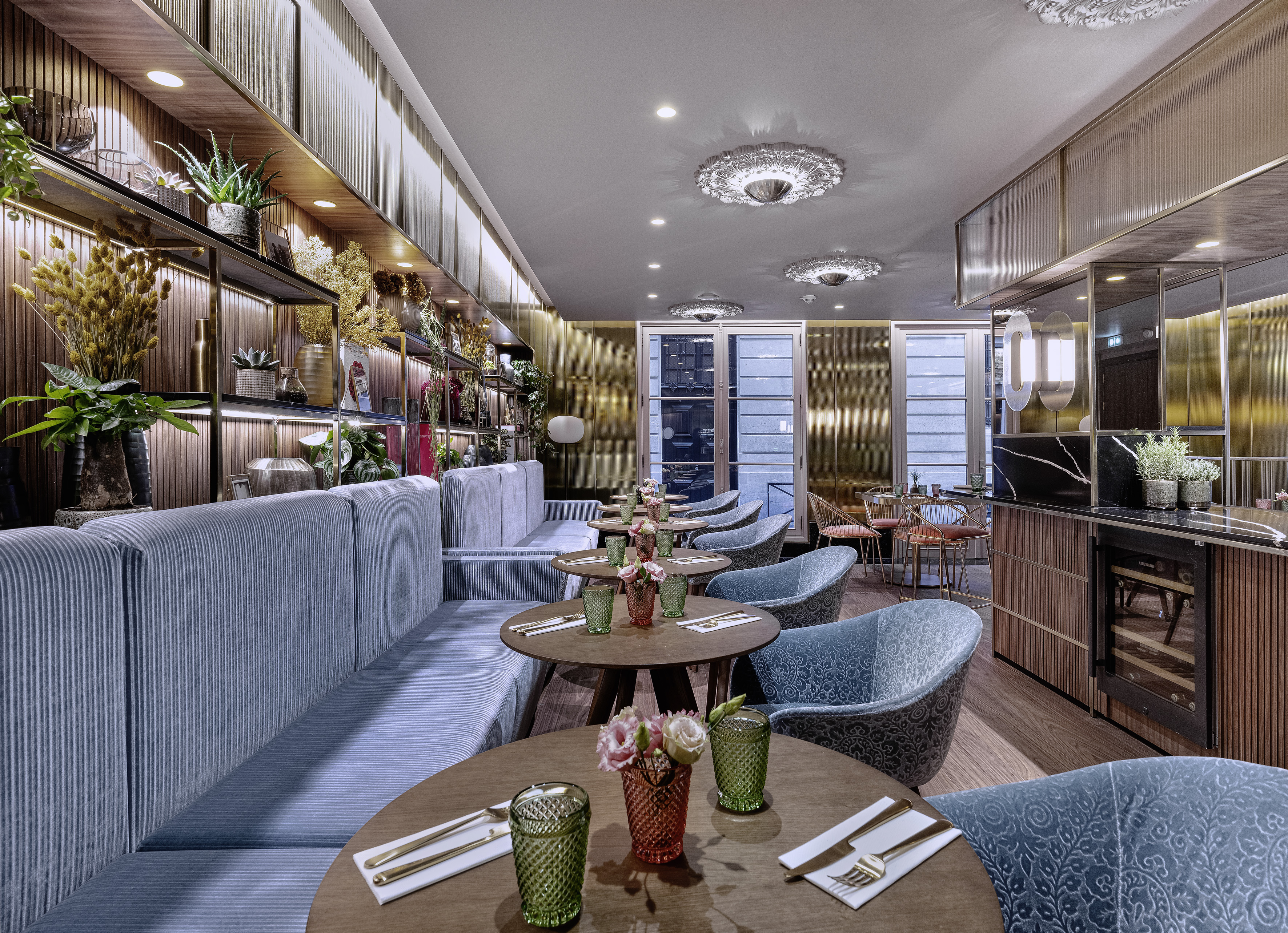 Stylish restaurant dining room with blue seating, wooden tables, and plant decor.