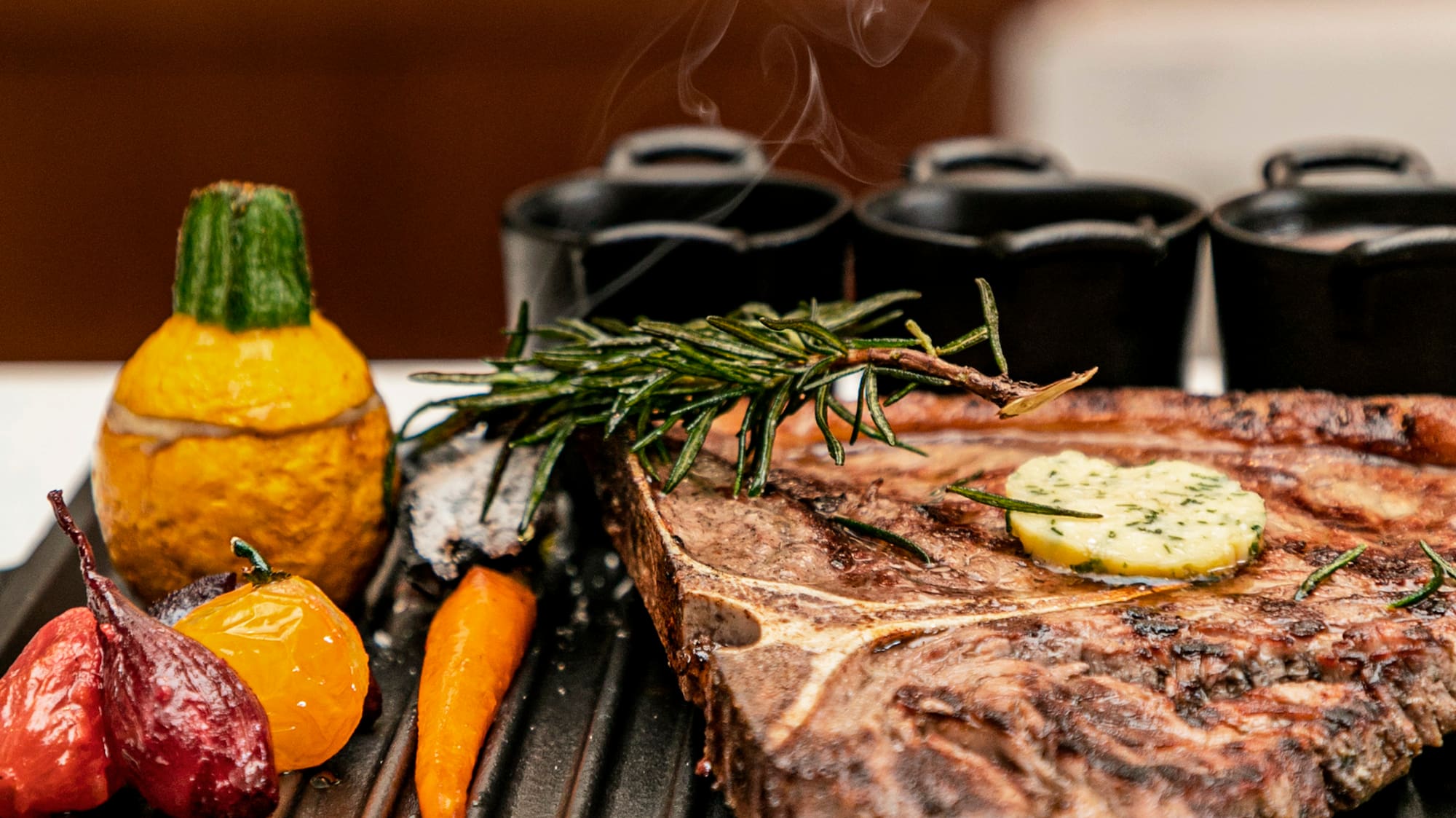 Smoking T-bone steak with herb butter, rosemary, and roasted vegetables on a grill.