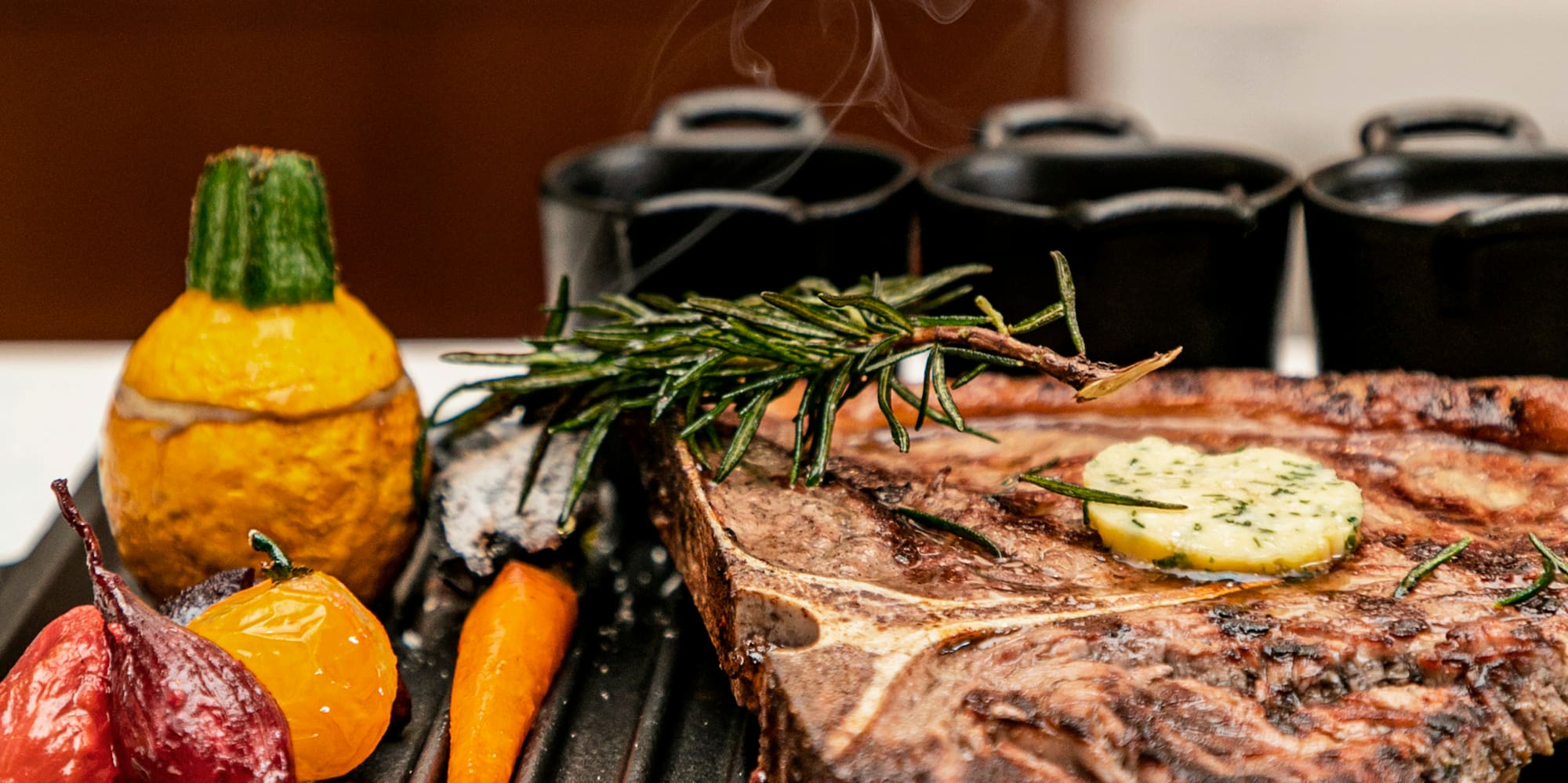 Smoking T-bone steak with herb butter, rosemary, and roasted vegetables on a grill.