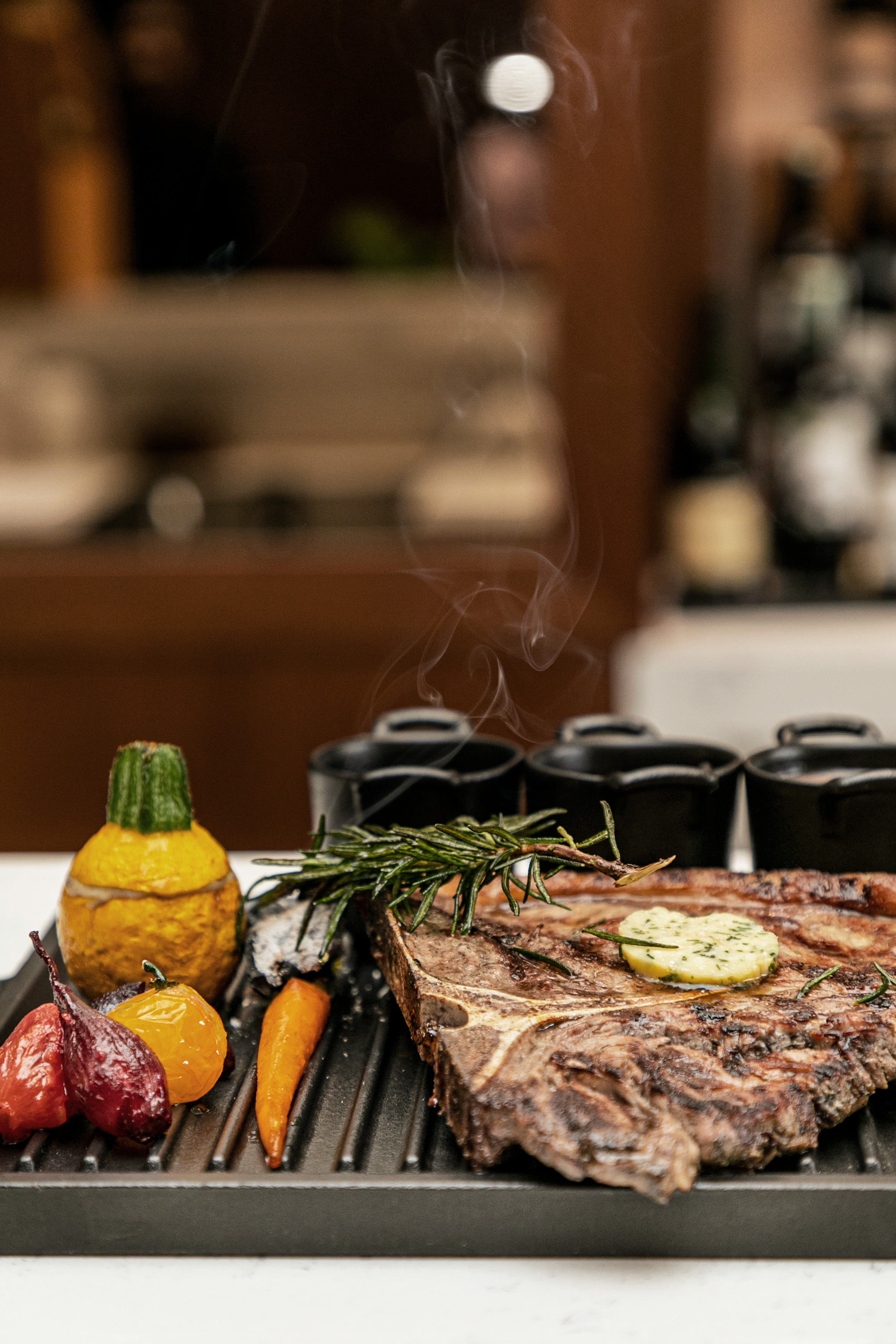 Smoking T-bone steak with herb butter, rosemary, and roasted vegetables on a grill.