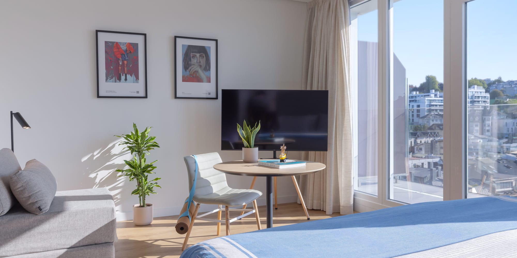 Apartamento luminoso con cama, sofá, ventanal y arte, vistas urbanas.