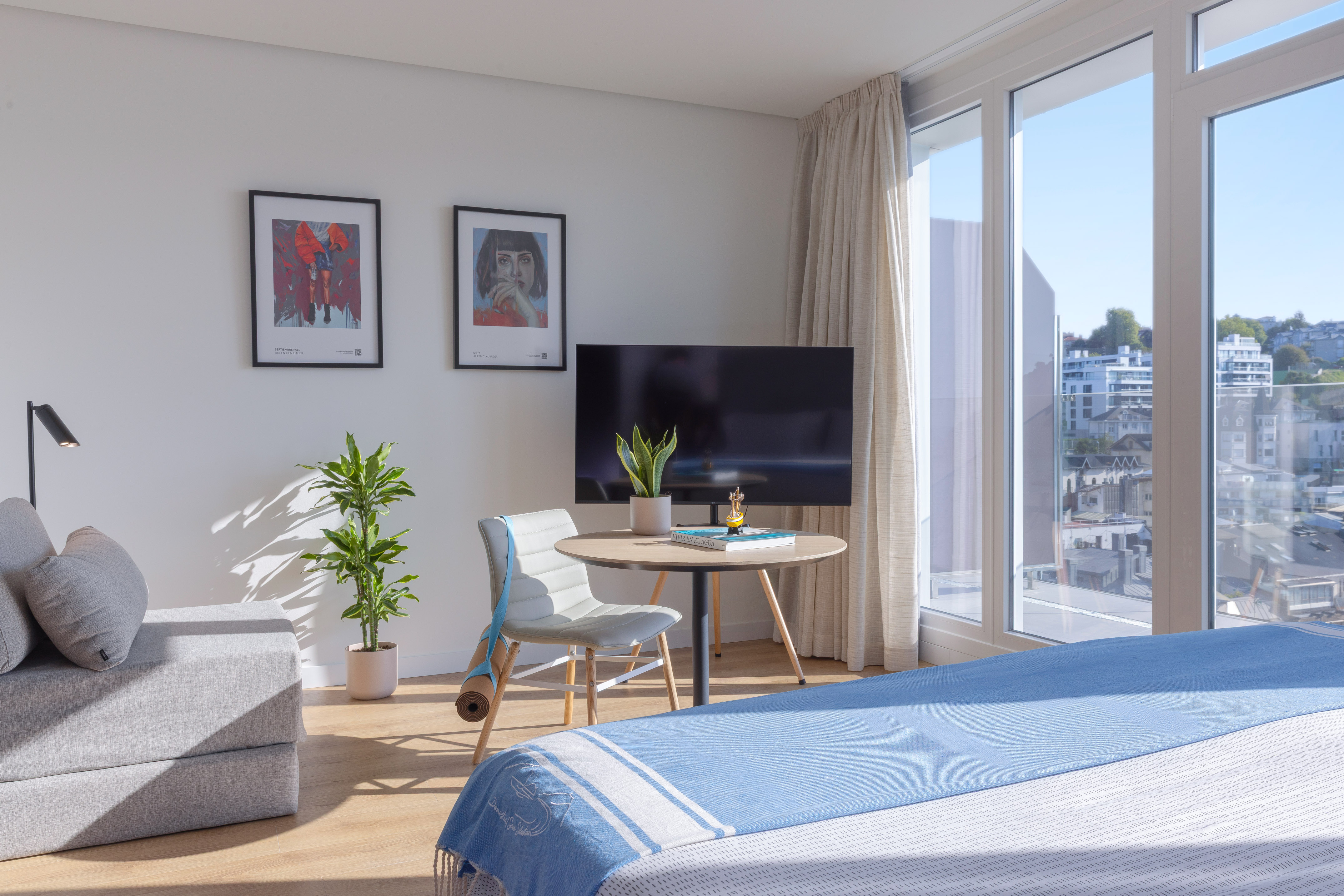 Apartamento luminoso con cama, sofá, ventanal y arte, vistas urbanas.