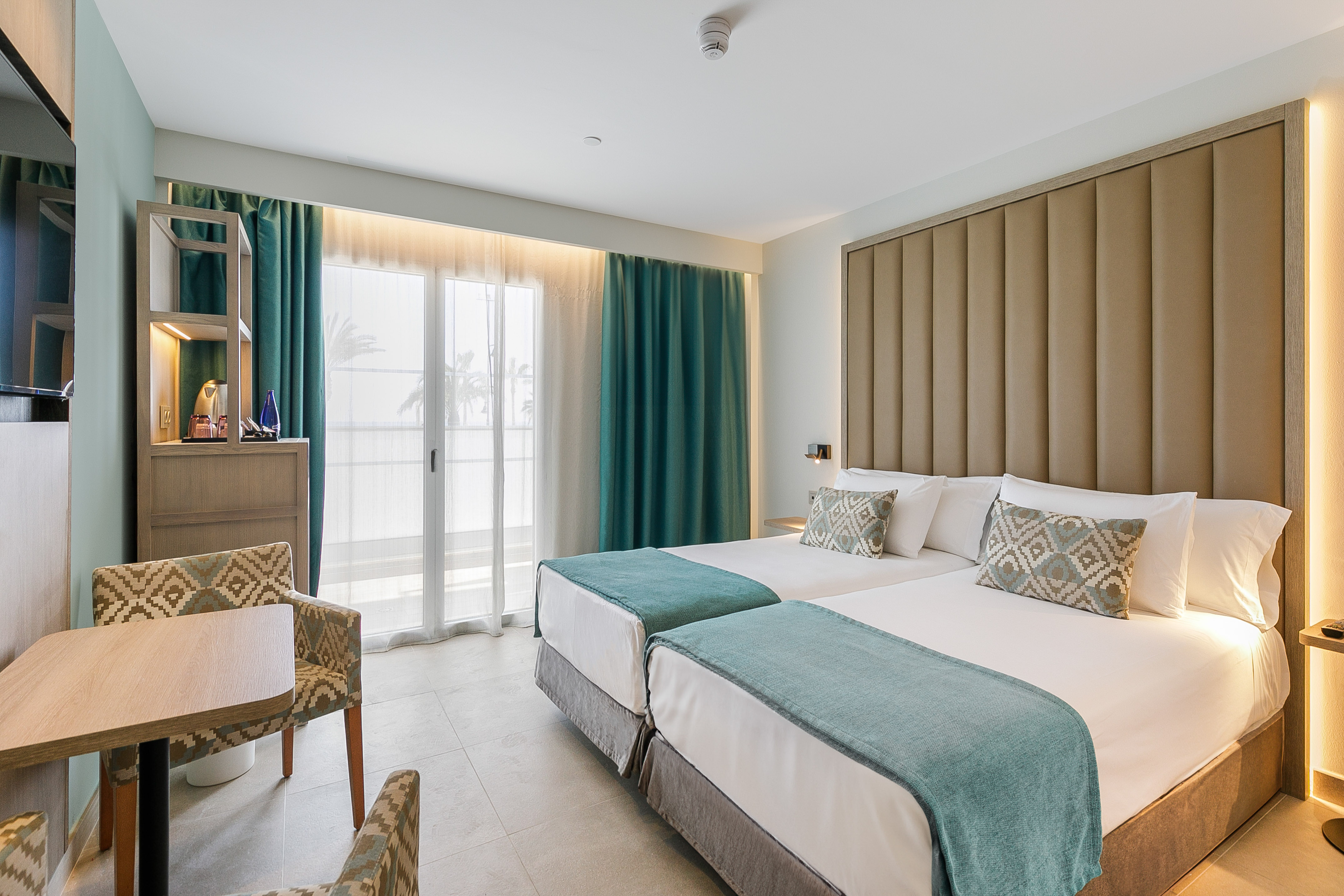 Bright hotel room with twin beds, modern decor, and balcony doors.