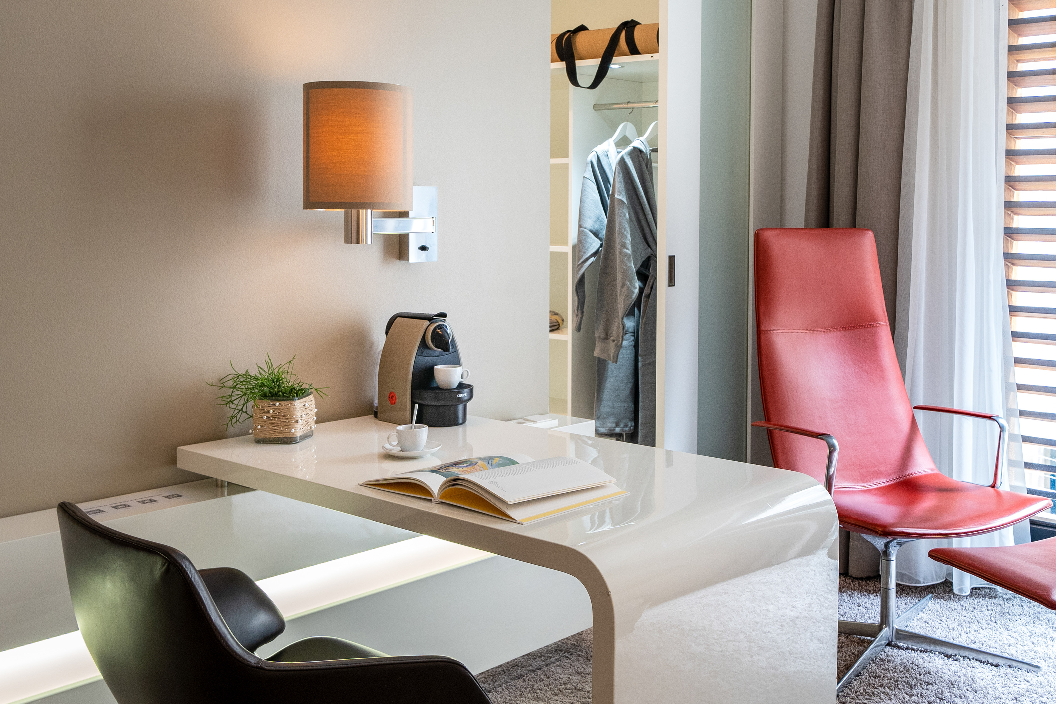 Contemporary hotel room workspace with desk, coffee machine, and red lounge chair.
