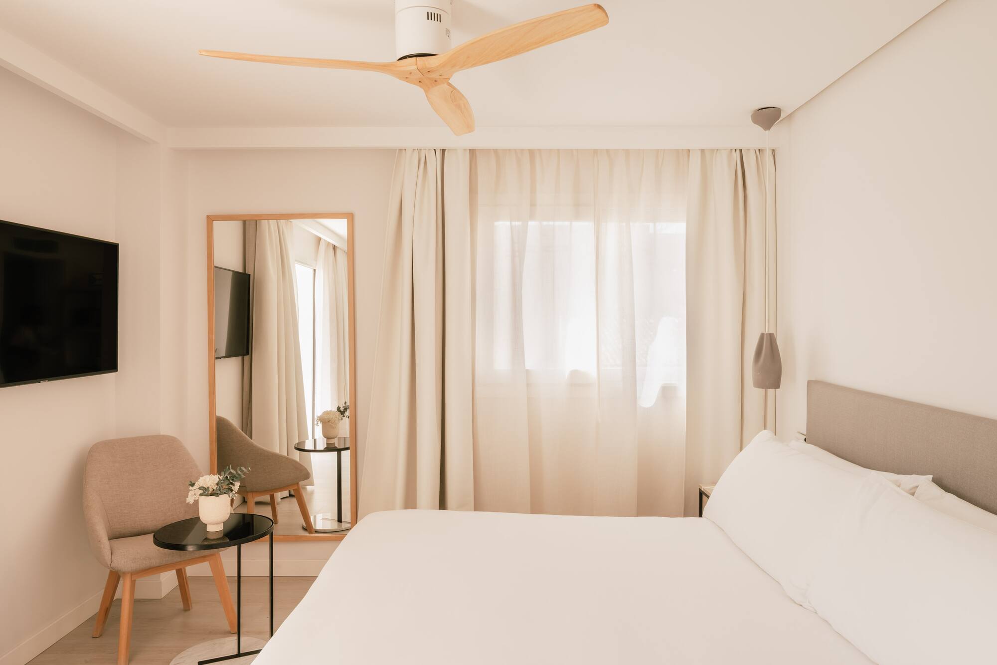 Habitación de hotel moderna. Cama blanca, ventilador de techo madera, TV y espejo.