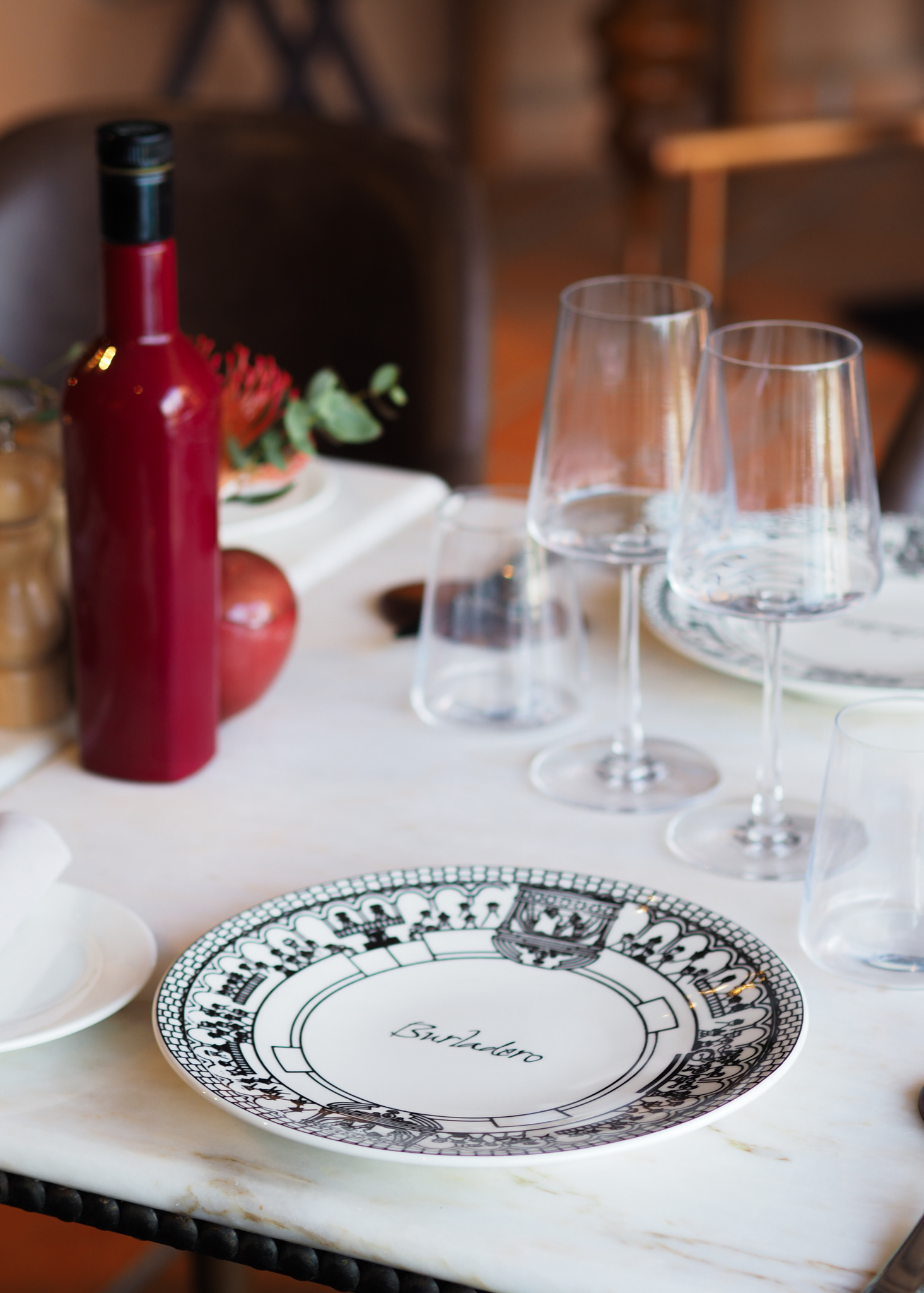 Restaurant table setting with Burladero plate, wine glasses, red bottle.
