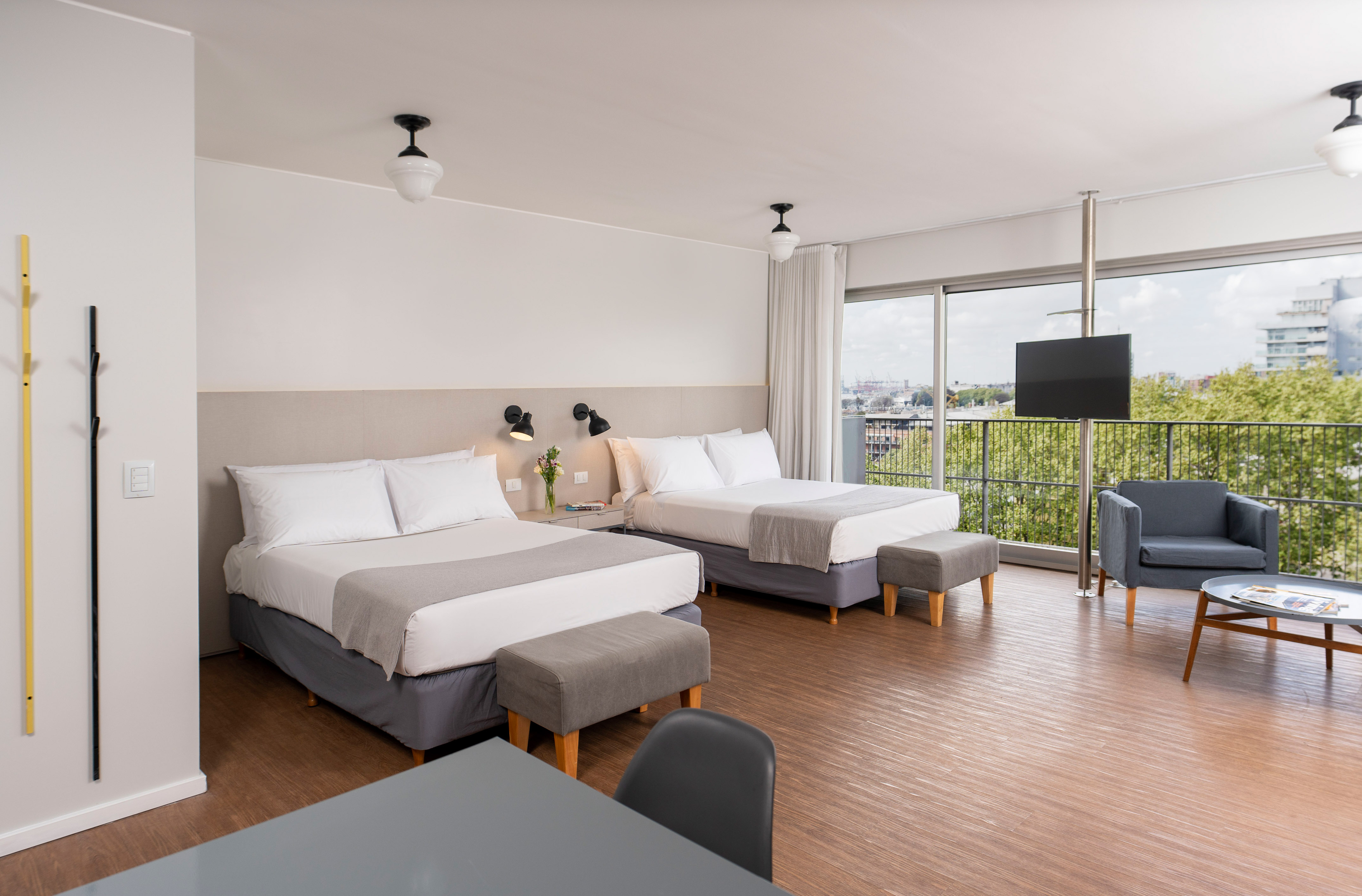 Modern hotel room with two beds, wooden floor, balcony, and city view.