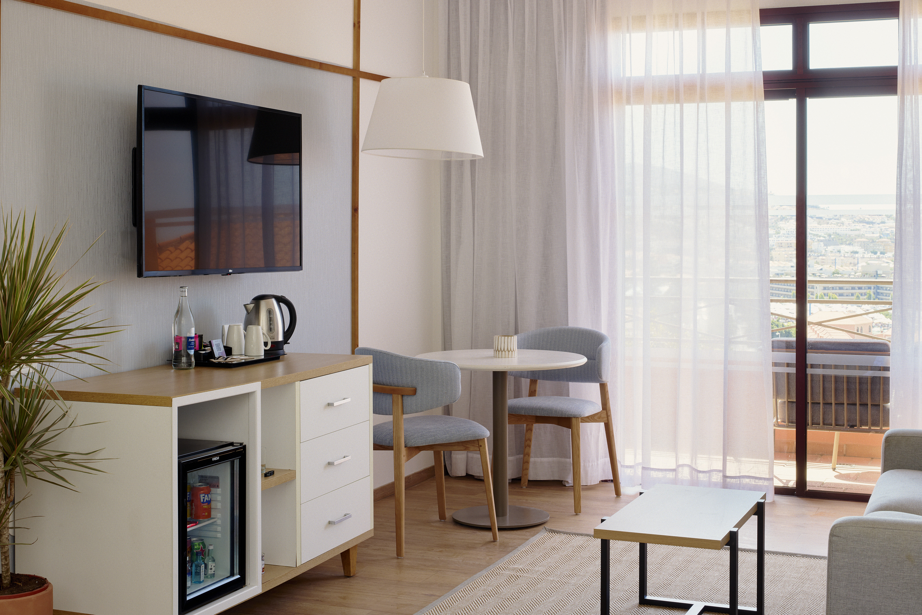 Modern hotel room with TV, minibar, seating area, and balcony city view.