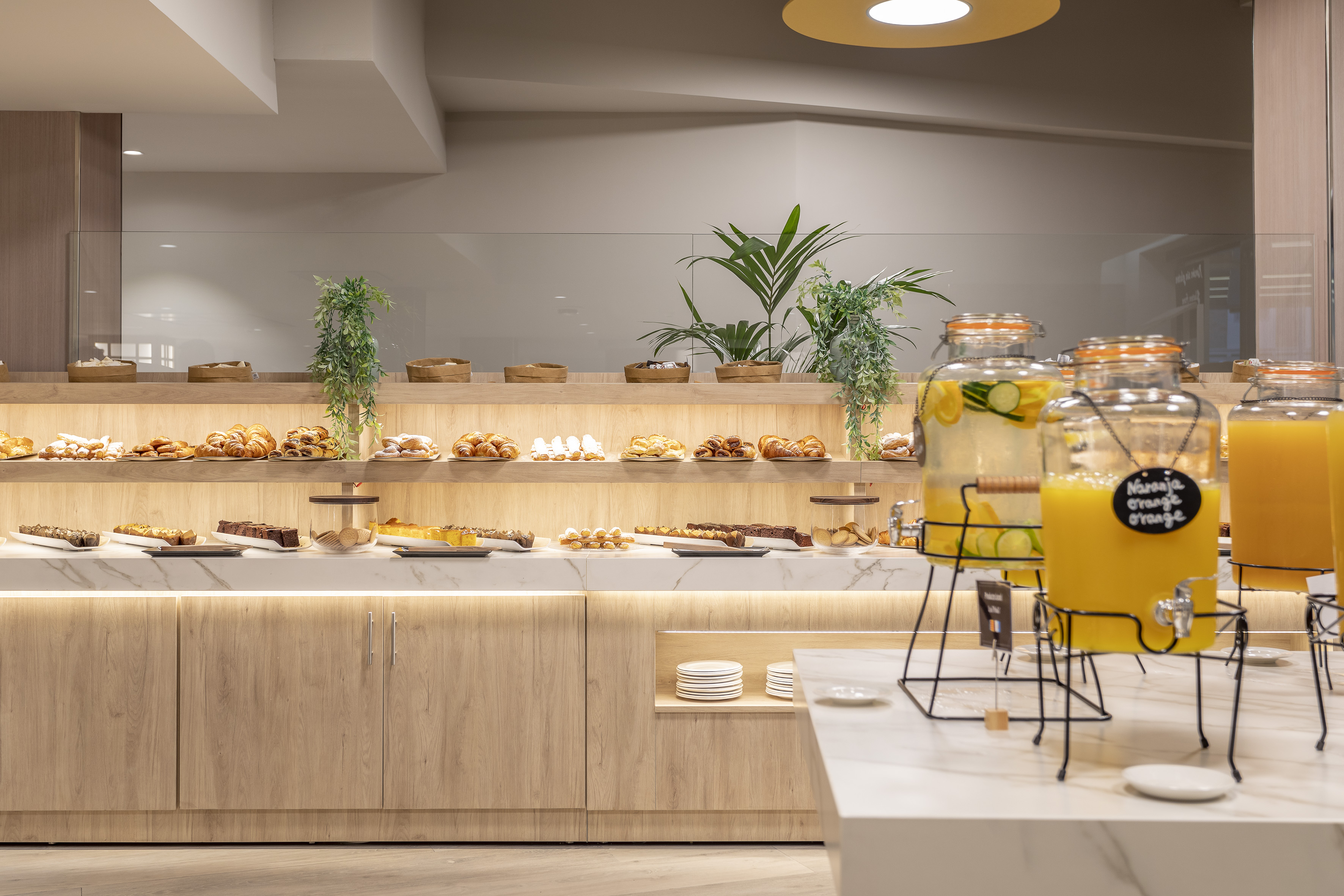 Hotel breakfast buffet with pastries, cakes, desserts, and fresh orange juice.