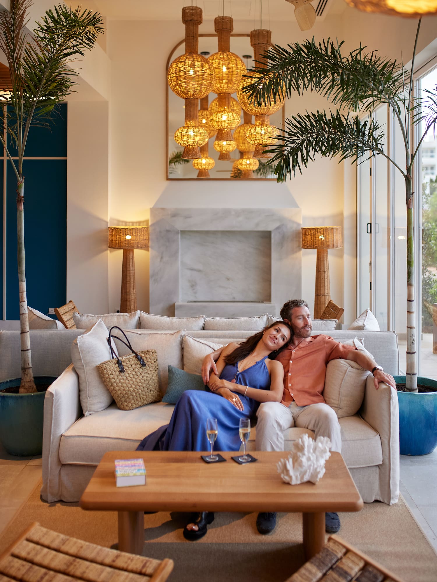 a man and woman sitting on a couch in a room with palm trees