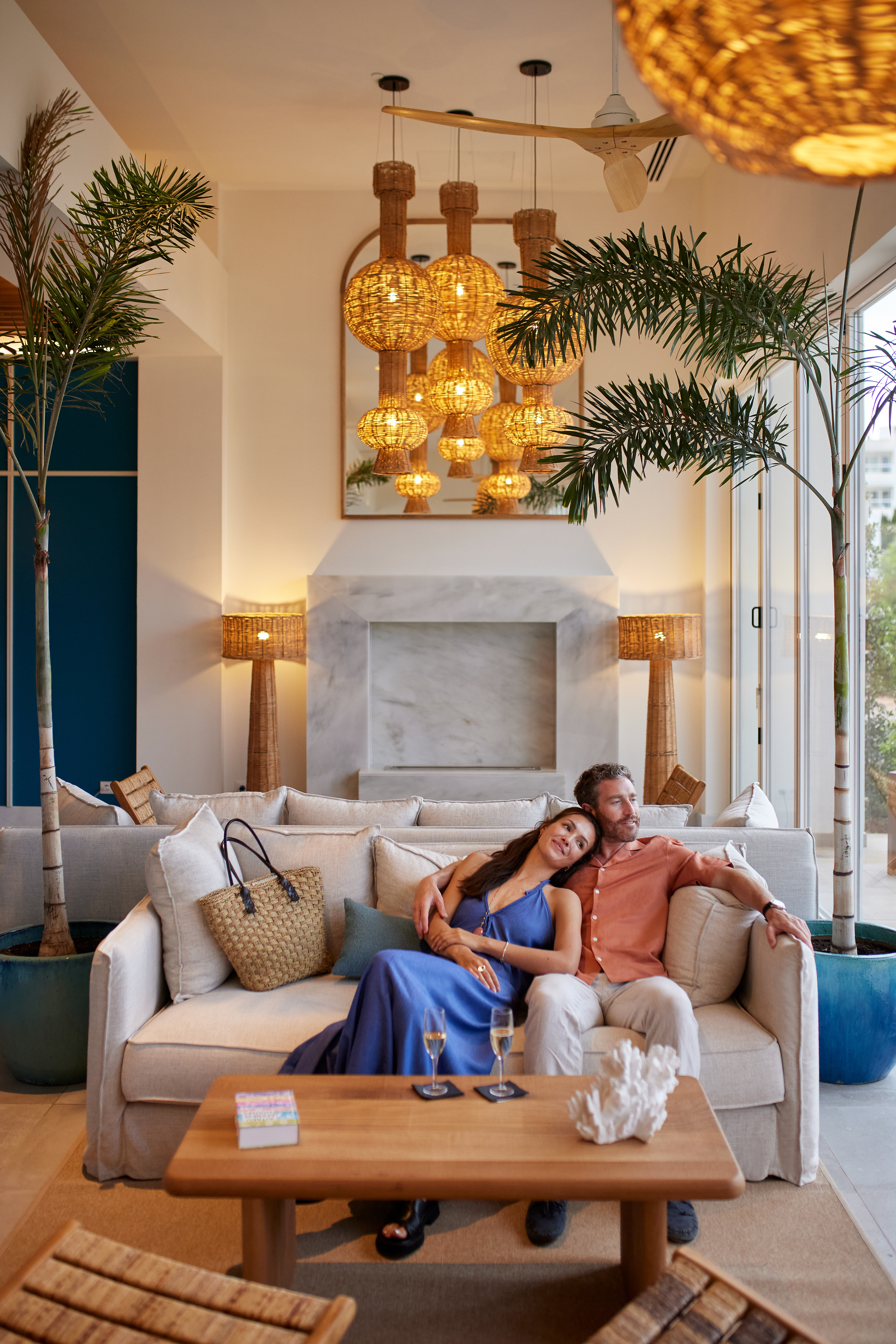 a man and woman sitting on a couch in a room with palm trees