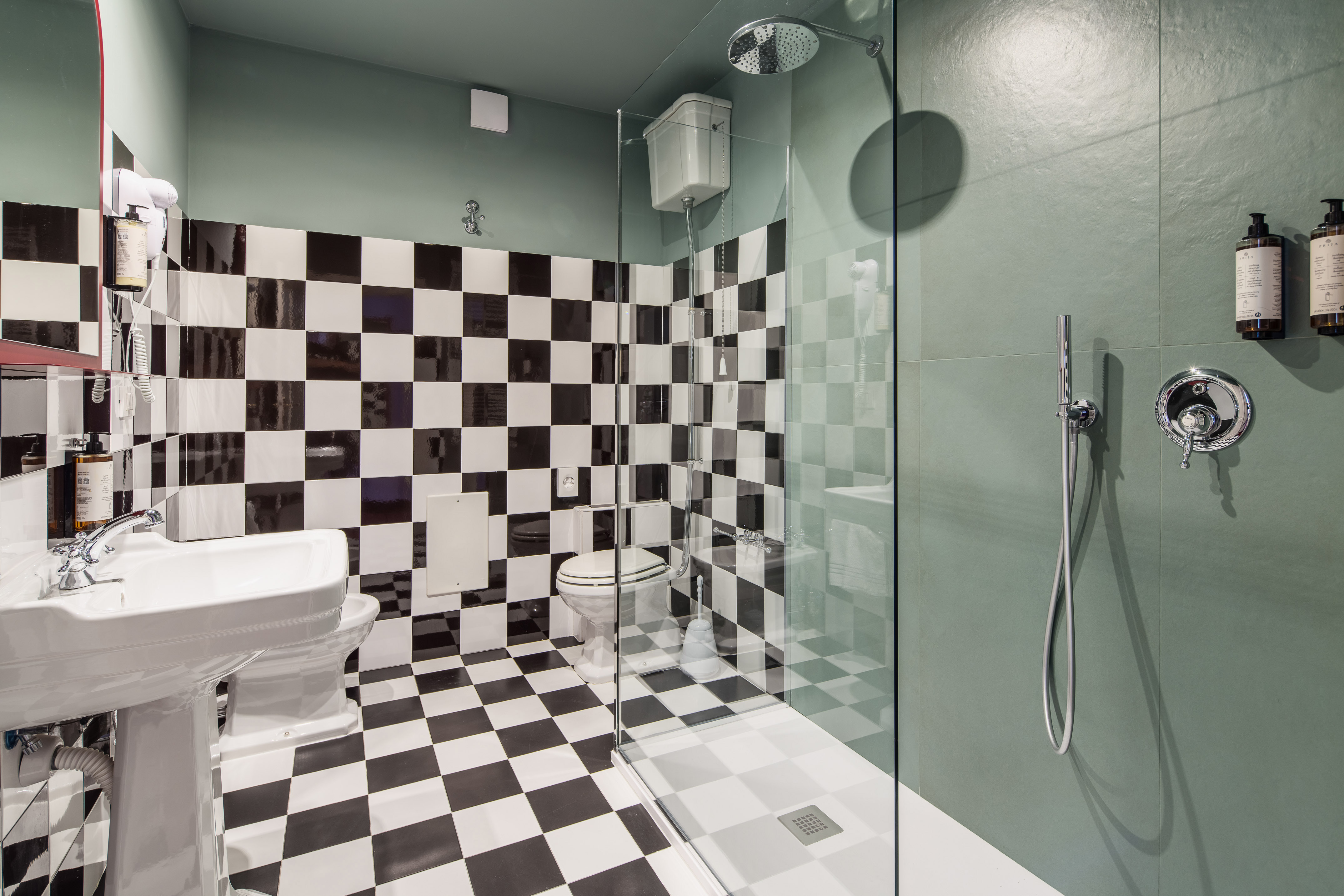 Bathroom with black and white checkerboard tiles, green walls, shower, toilet, and sink.