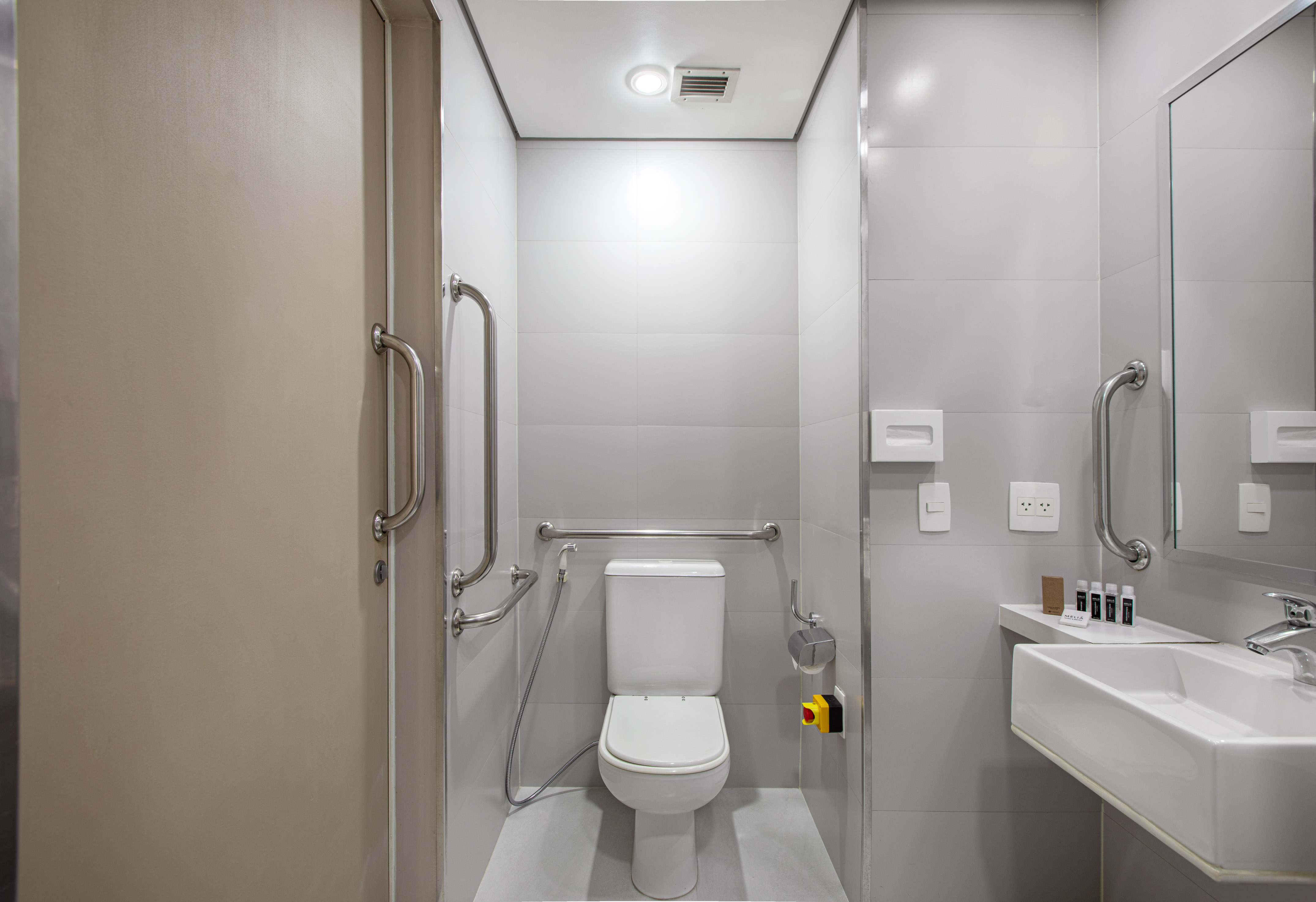Modern accessible bathroom with white toilet, grab bars, and sink.
