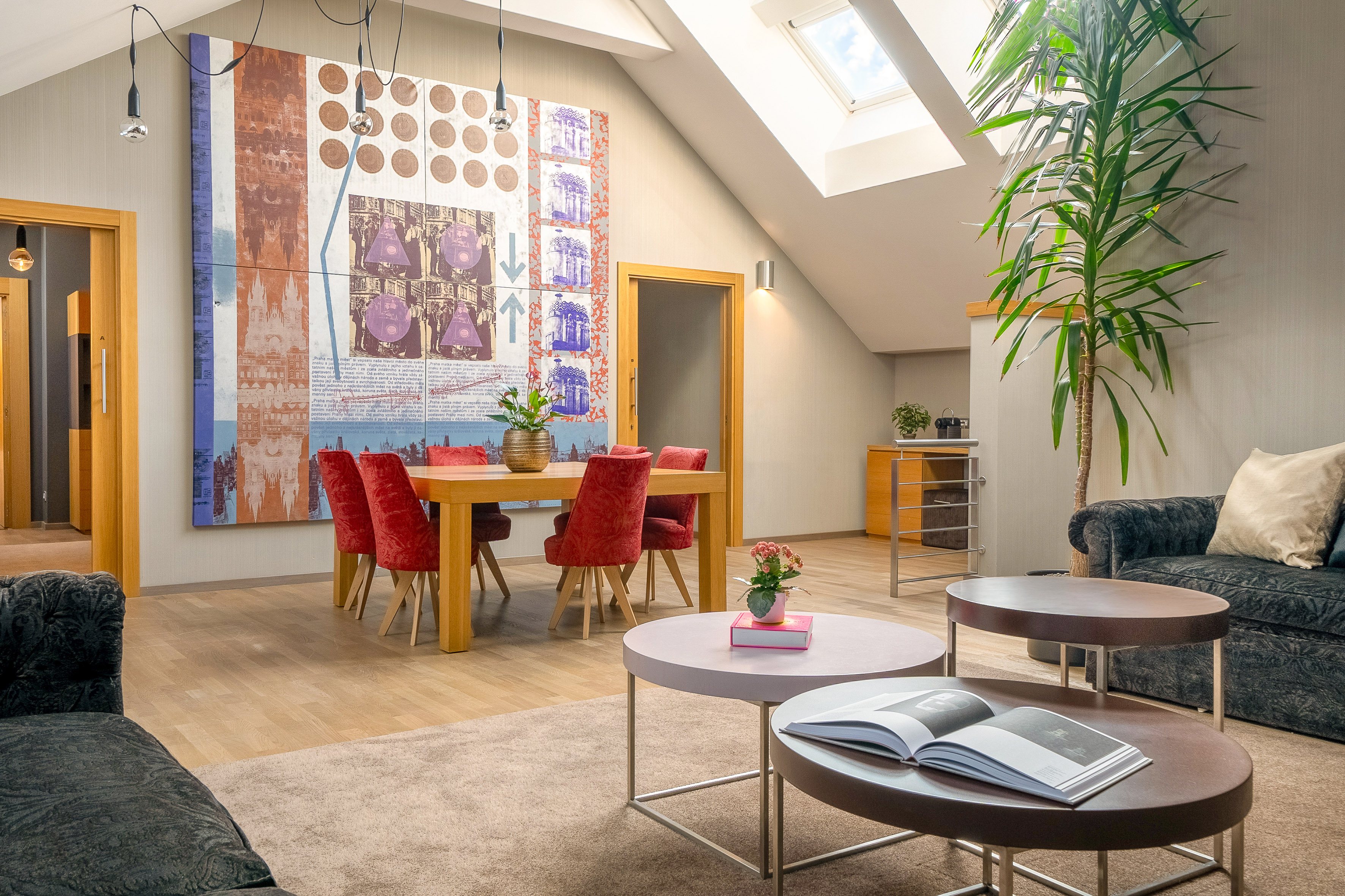 Modern living dining room with large graphic wall art, red chairs, and skylight.