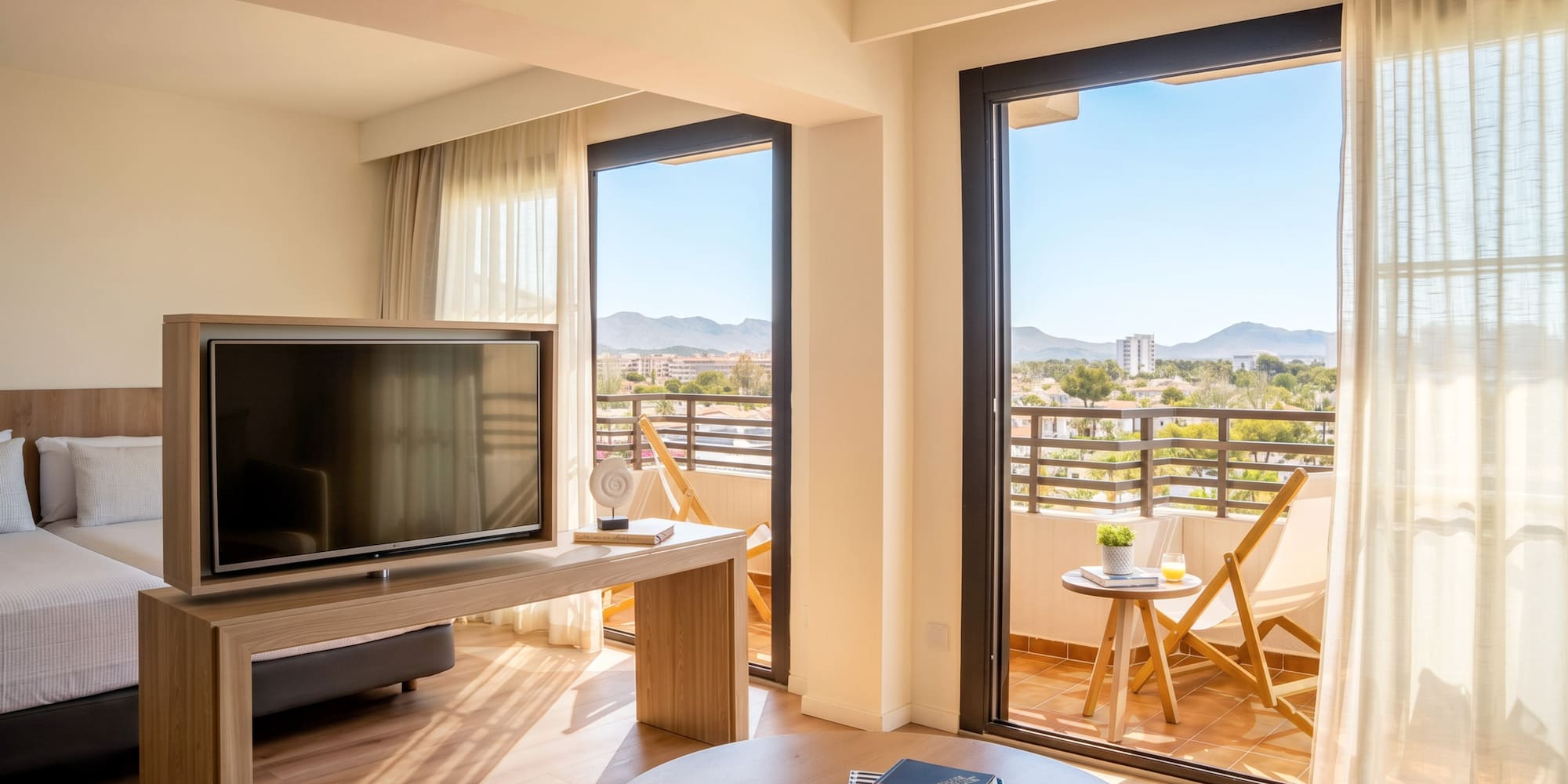 Bright hotel suite with balcony, TV, and scenic mountain views.