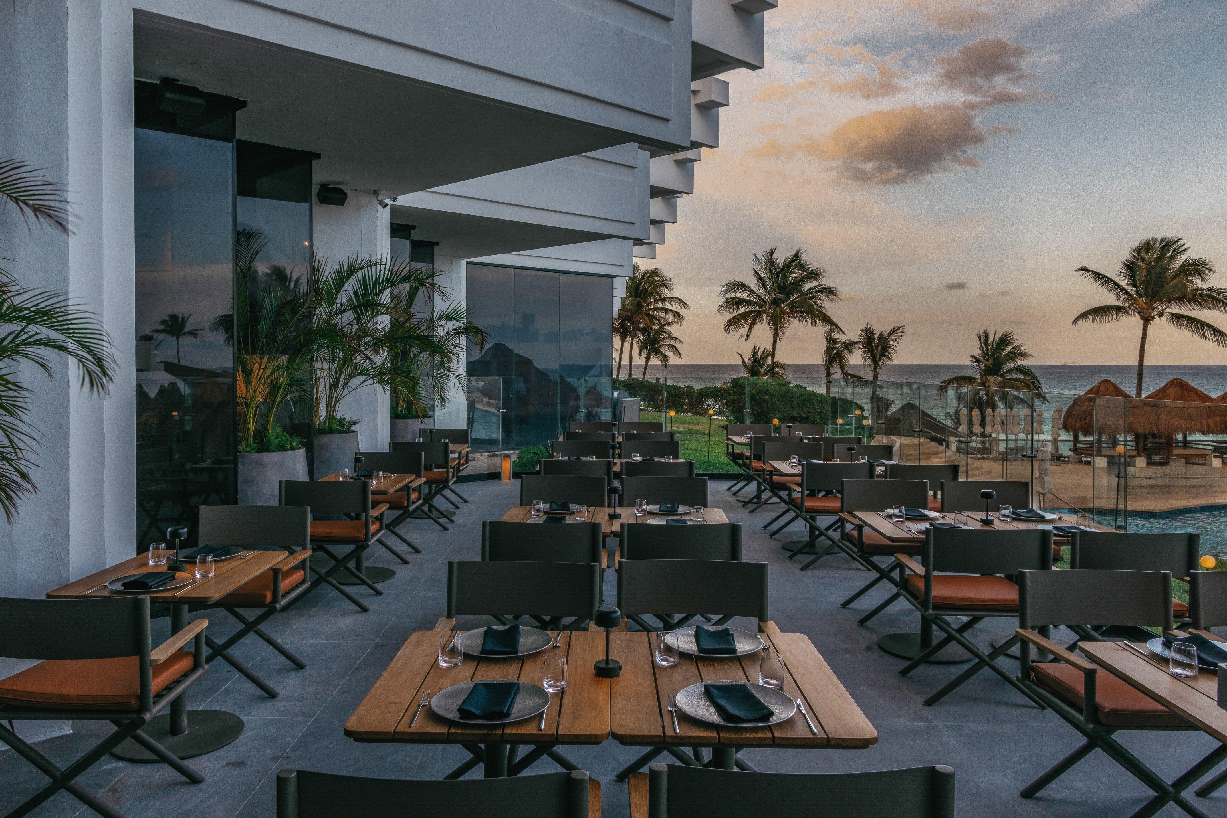 Luxury outdoor restaurant patio with ocean view, palm trees, and sunset.
