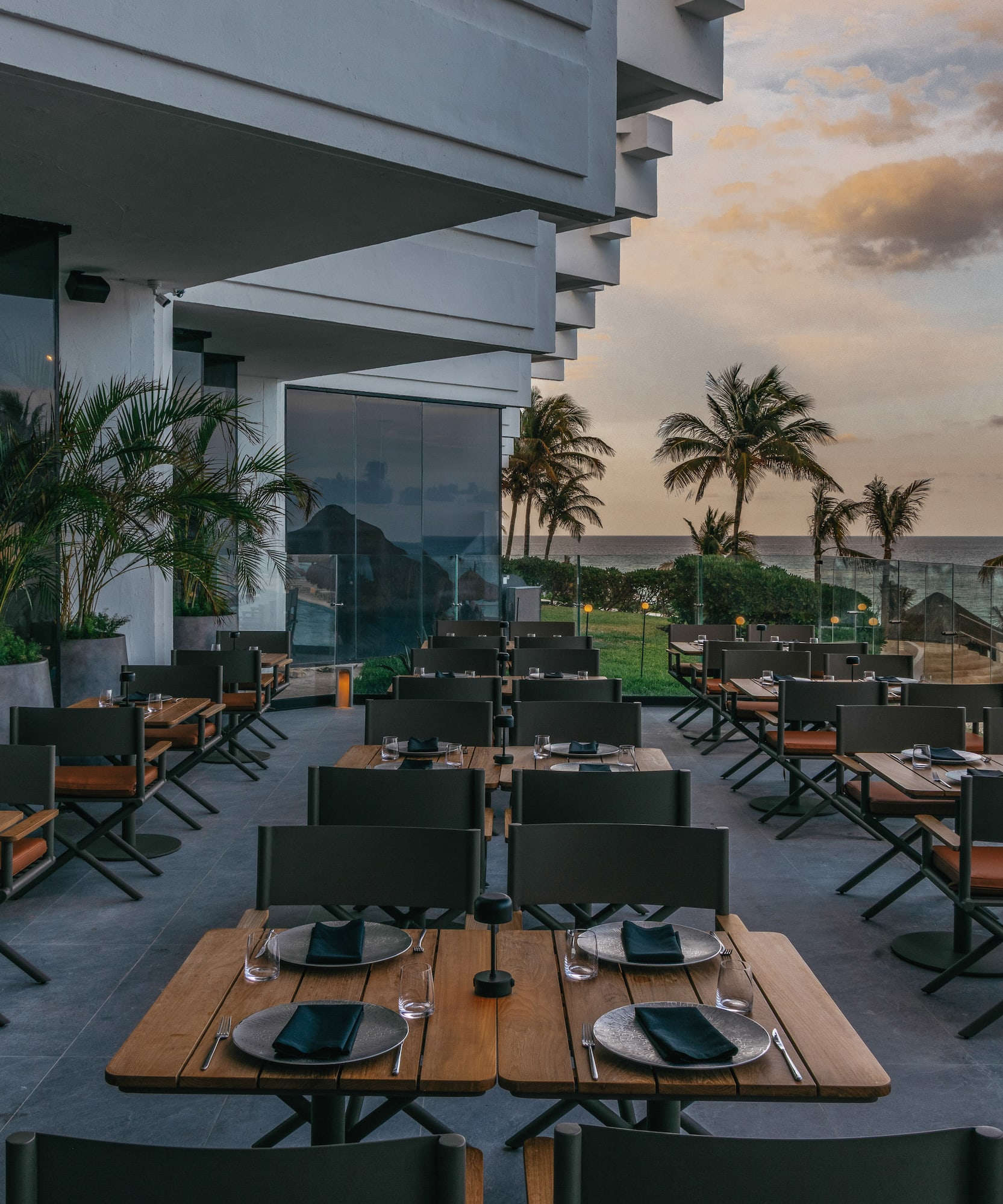 Luxury outdoor restaurant patio with ocean view, palm trees, and sunset.
