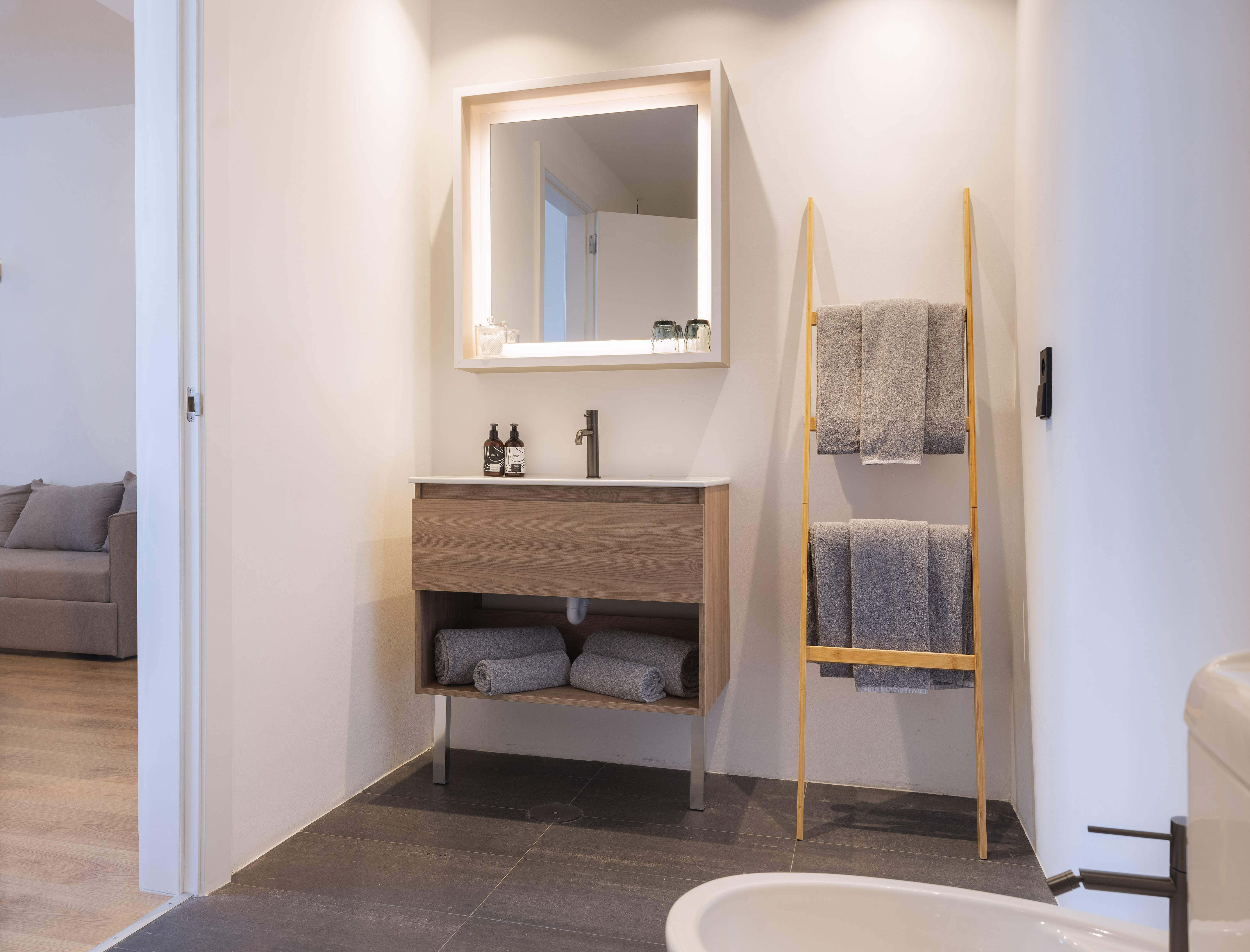Modern bathroom with wood vanity, lighted mirror, and bamboo towel rack.