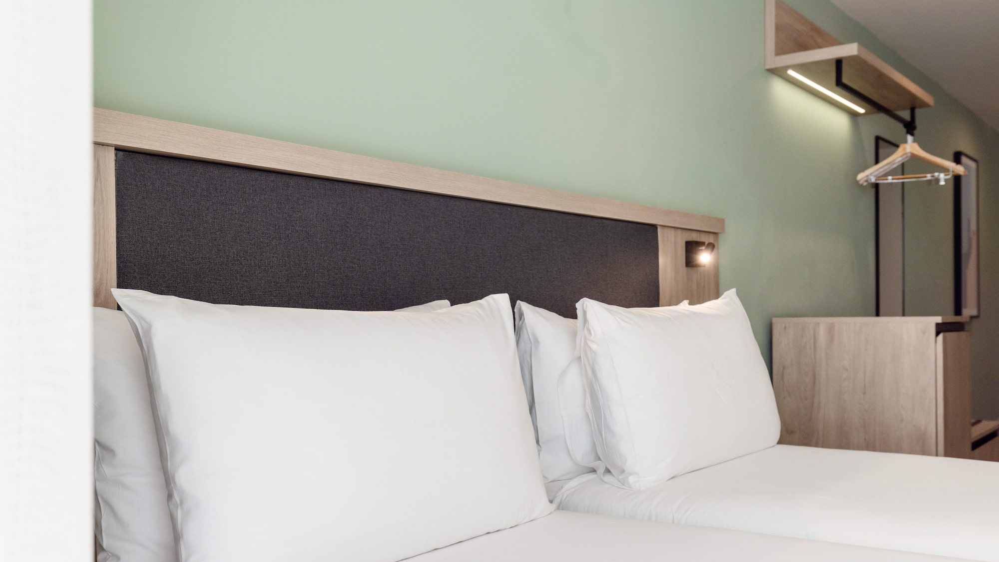 Modern hotel bedroom with white bed, wooden headboard, light green wall.
