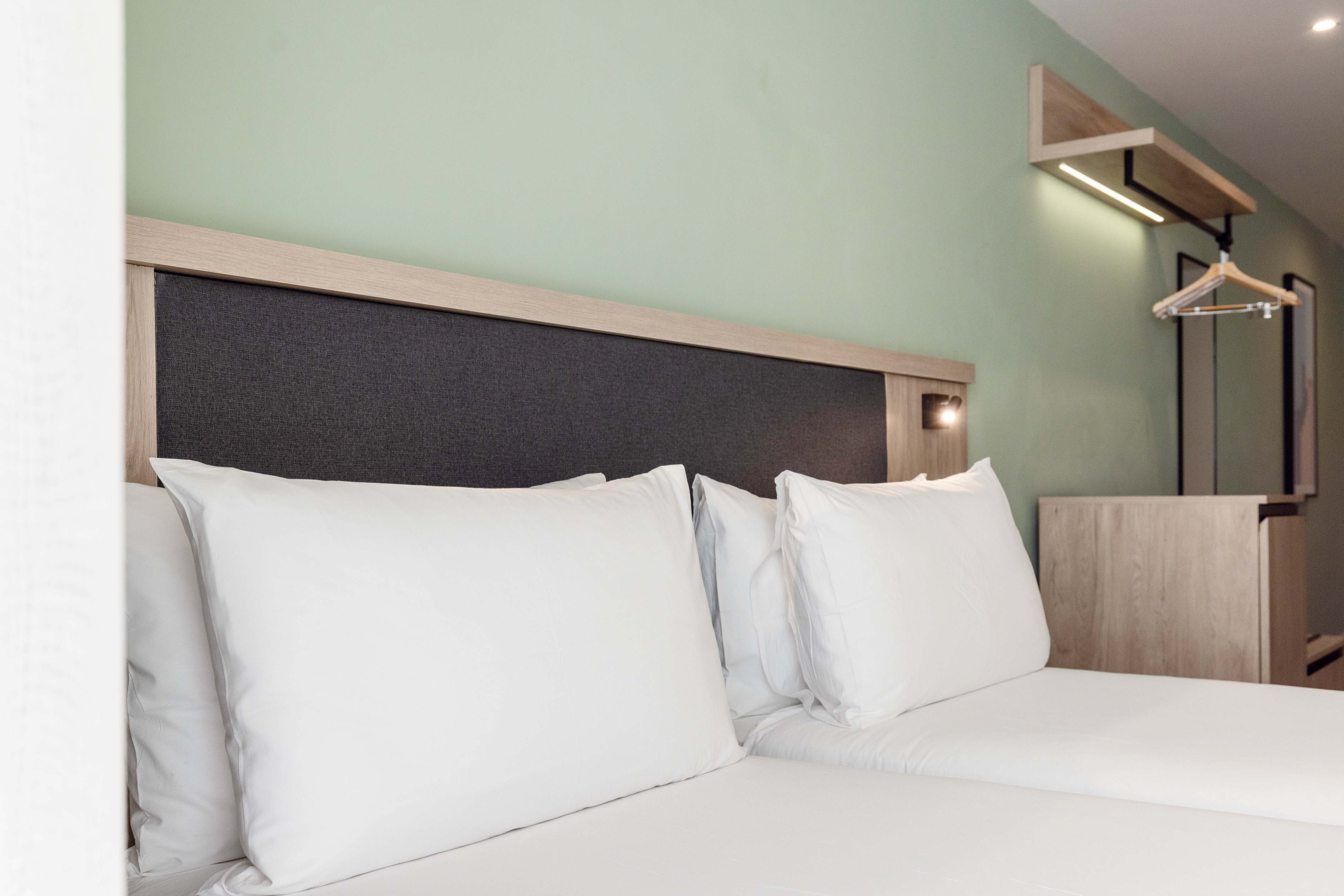 Modern hotel bedroom with white bed, wooden headboard, light green wall.