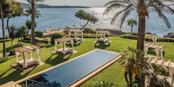 a pool in a grassy area with palm trees and a body of water.