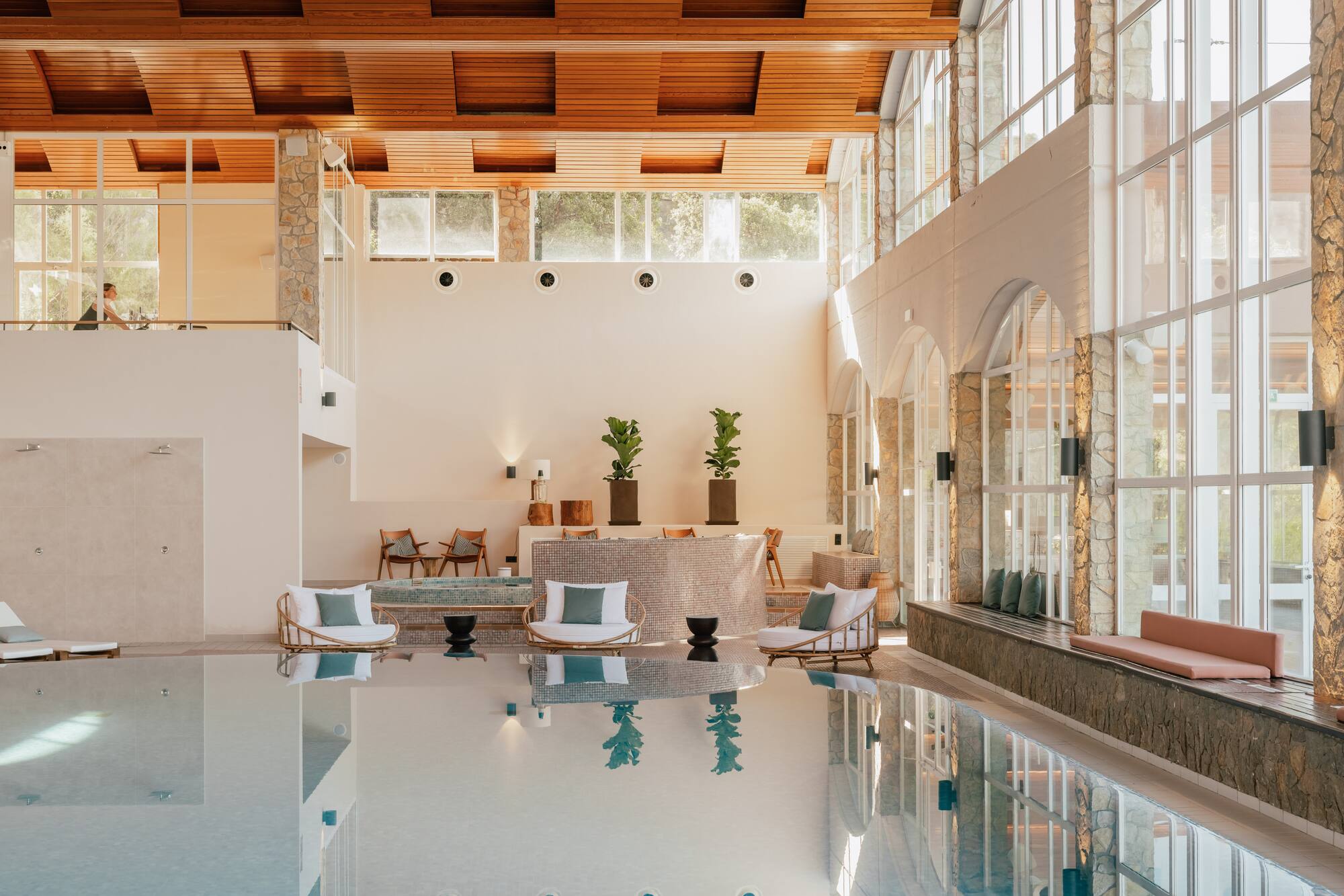 Luxury resort indoor pool with wooden ceiling, large windows, and elegant seating.