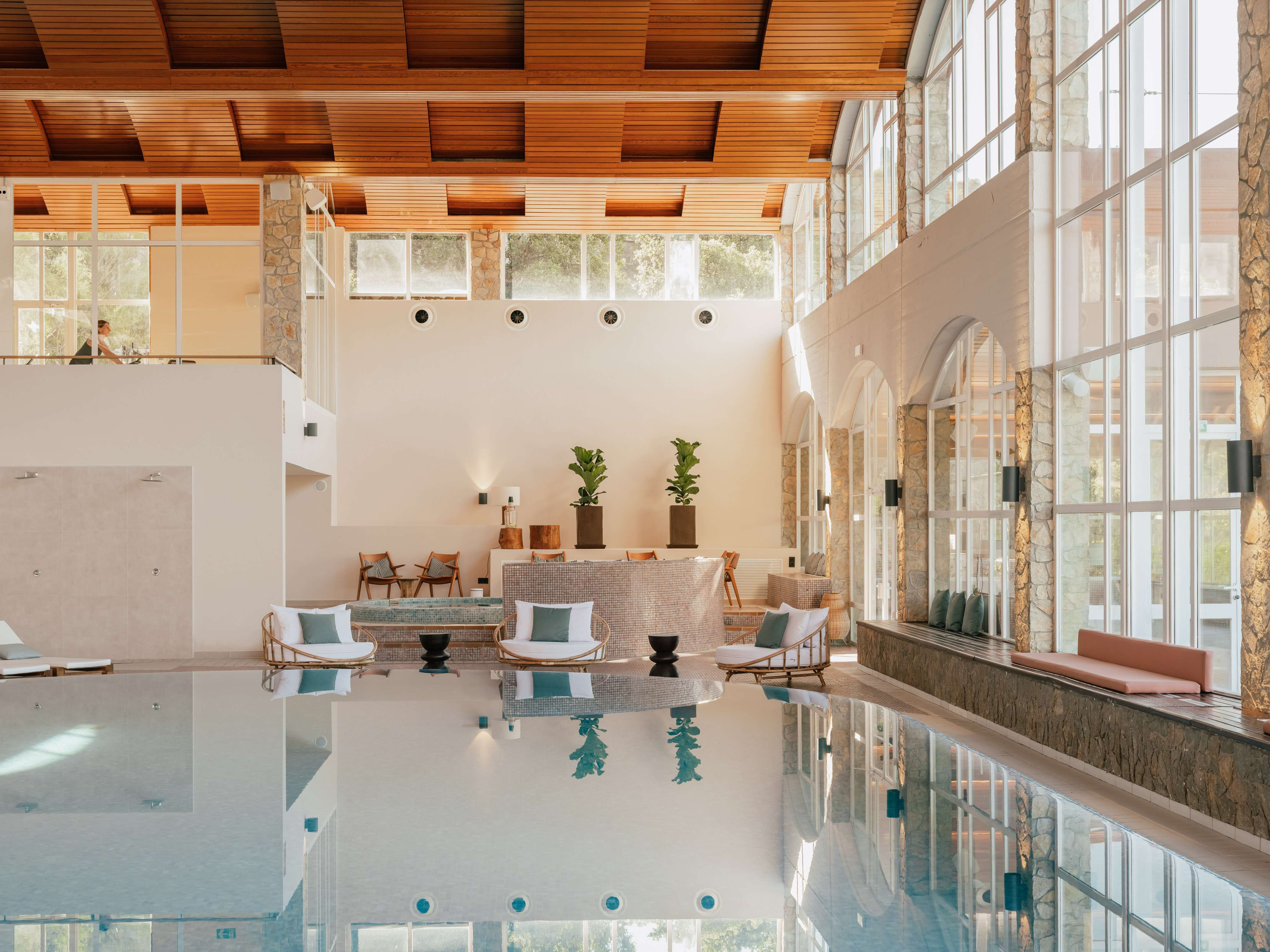 Luxury resort indoor pool with wooden ceiling, large windows, and elegant seating.