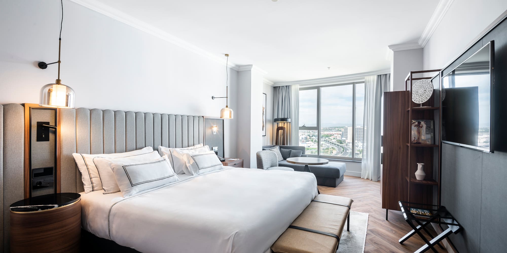 Moderna suite de hotel con cama grande, zona de estar y vistas a la ciudad.