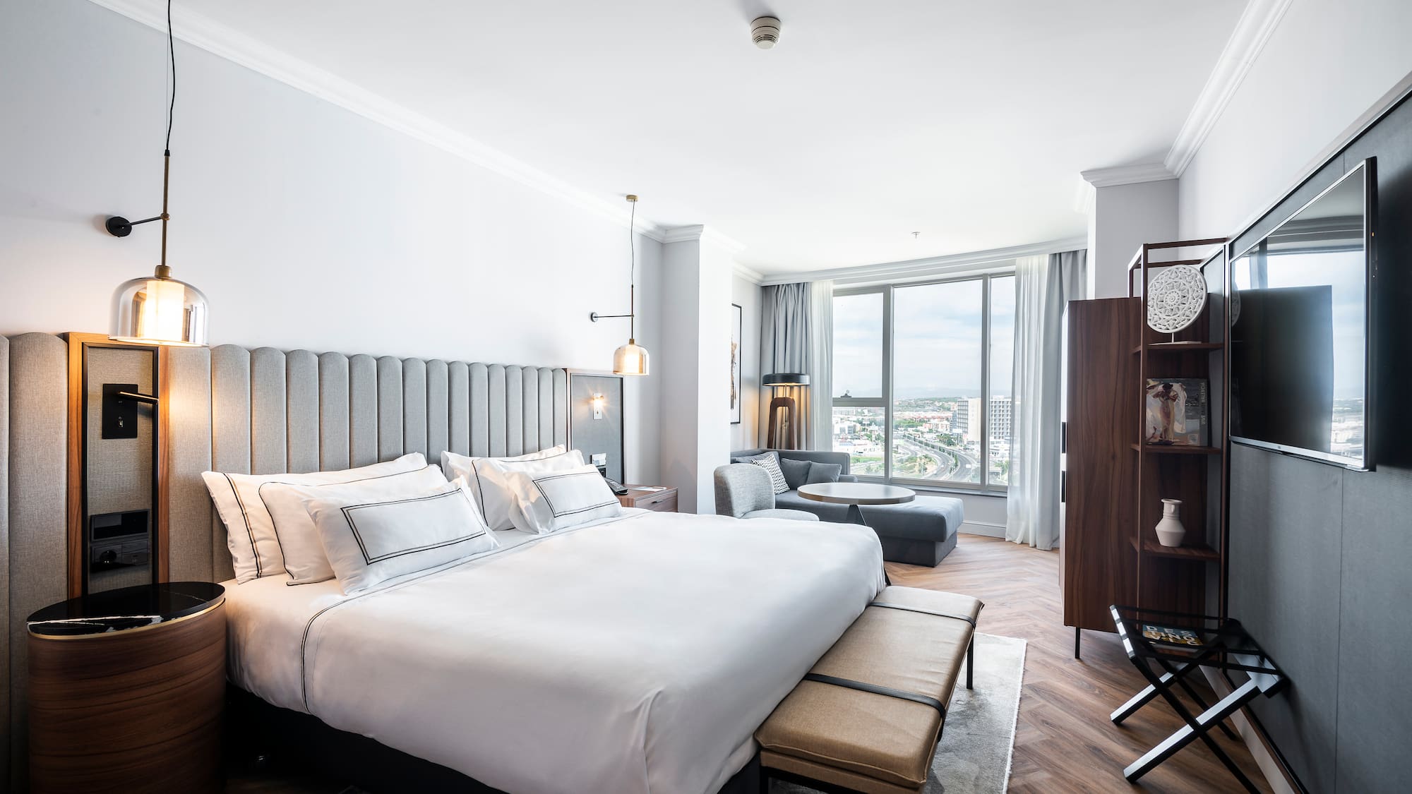 Moderna suite de hotel con cama grande, zona de estar y vistas a la ciudad.