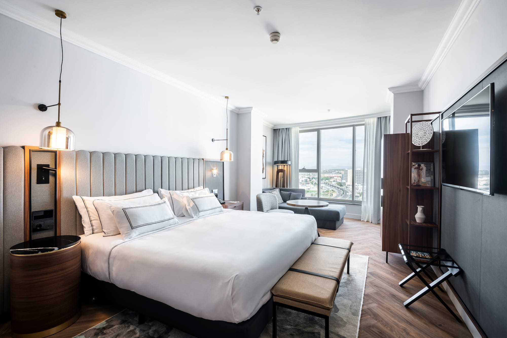 Moderna suite de hotel con cama grande, zona de estar y vistas a la ciudad.