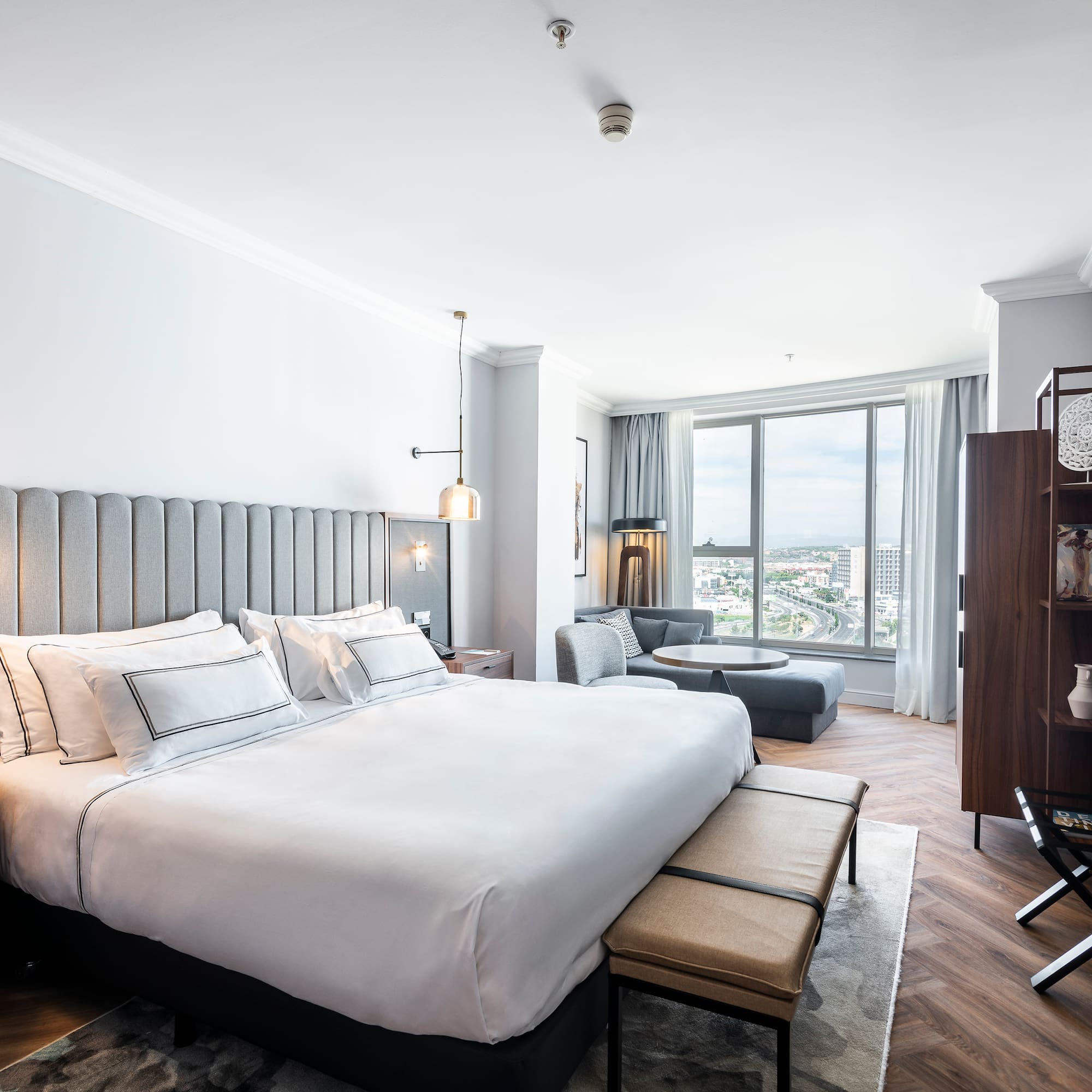 Moderna suite de hotel con cama grande, zona de estar y vistas a la ciudad.