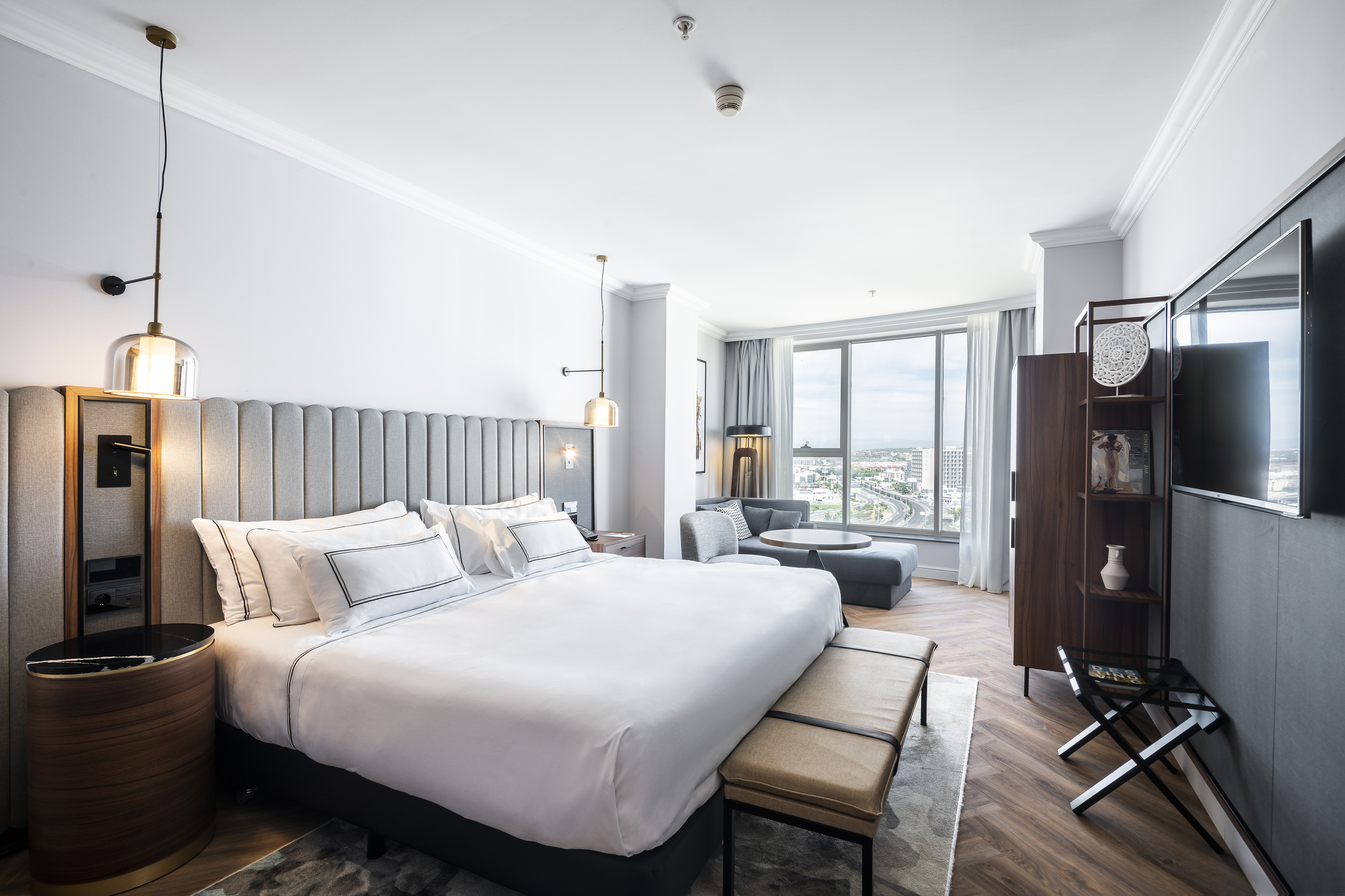 Moderna suite de hotel con cama grande, zona de estar y vistas a la ciudad.
