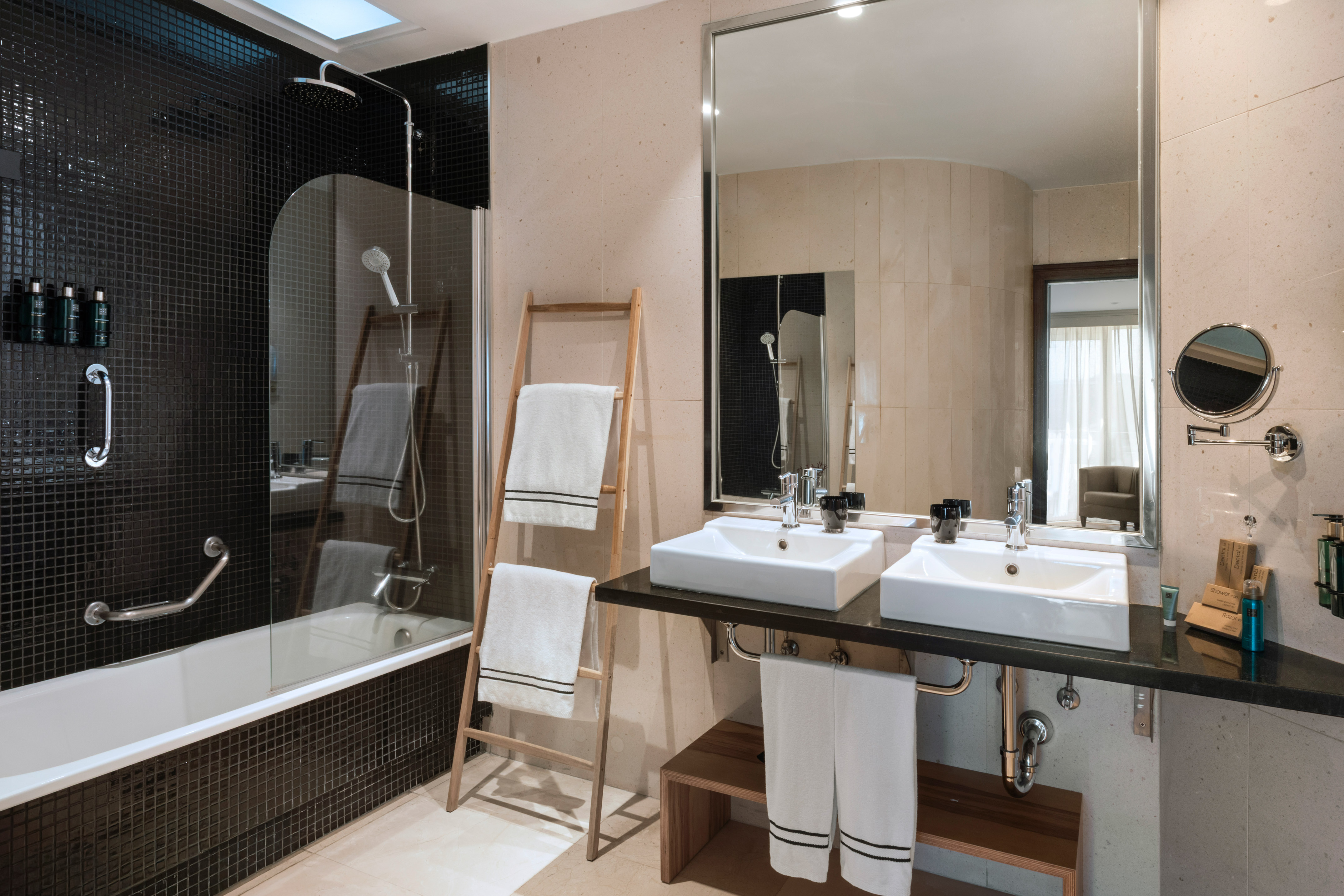 Modern hotel bathroom with black tiled shower, double vanity, and white towels.