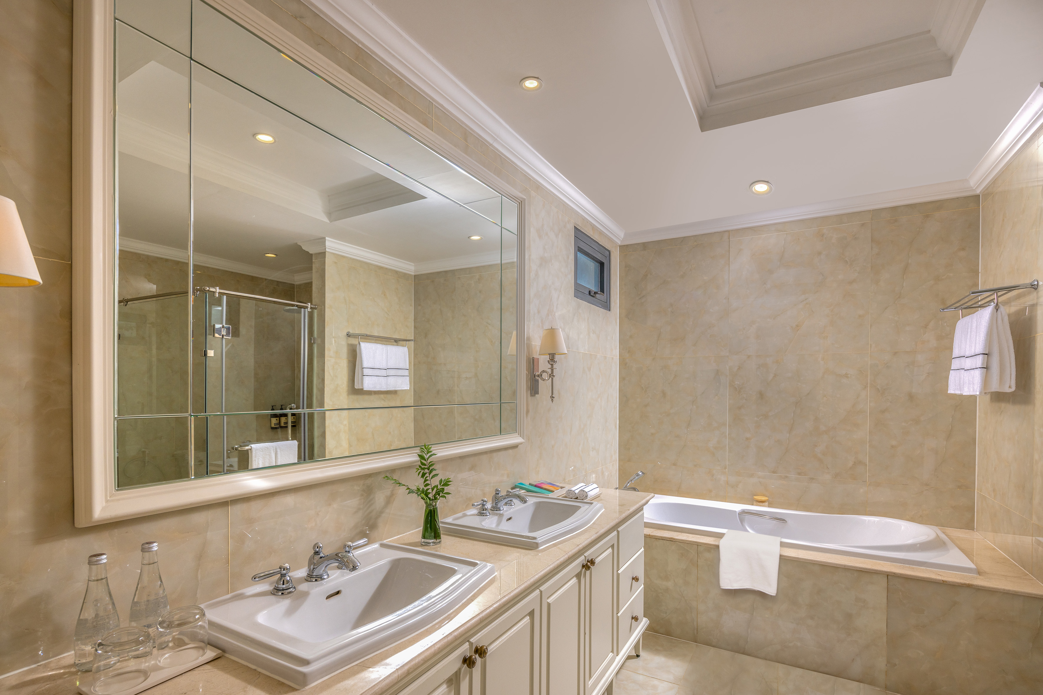 Elegant hotel bathroom with double vanity, large mirror, bathtub, and glass shower.